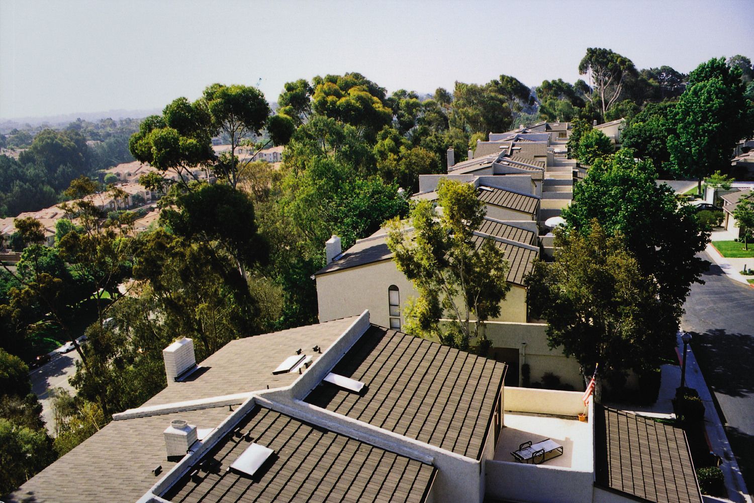 Row of white houses with brown roofs nestled among green trees on a hillside.