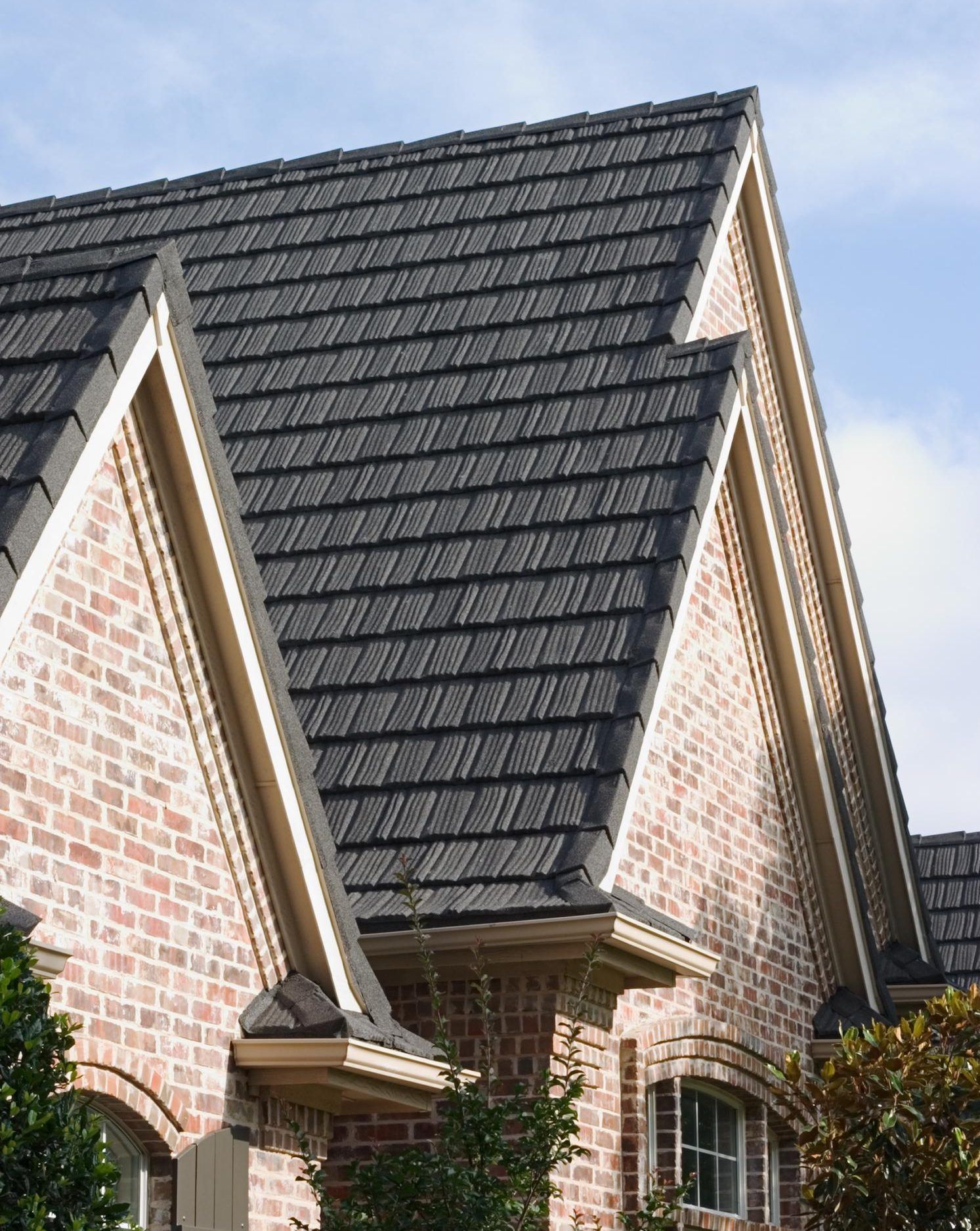 Brick house with a dark gray metal tile roof and tan trim.
