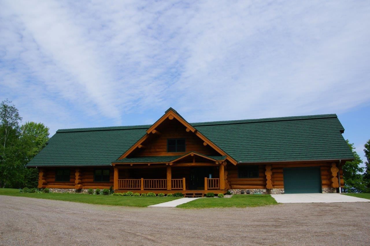 Log cabin with green roof, porch, and attached garage under a partly cloudy sky.