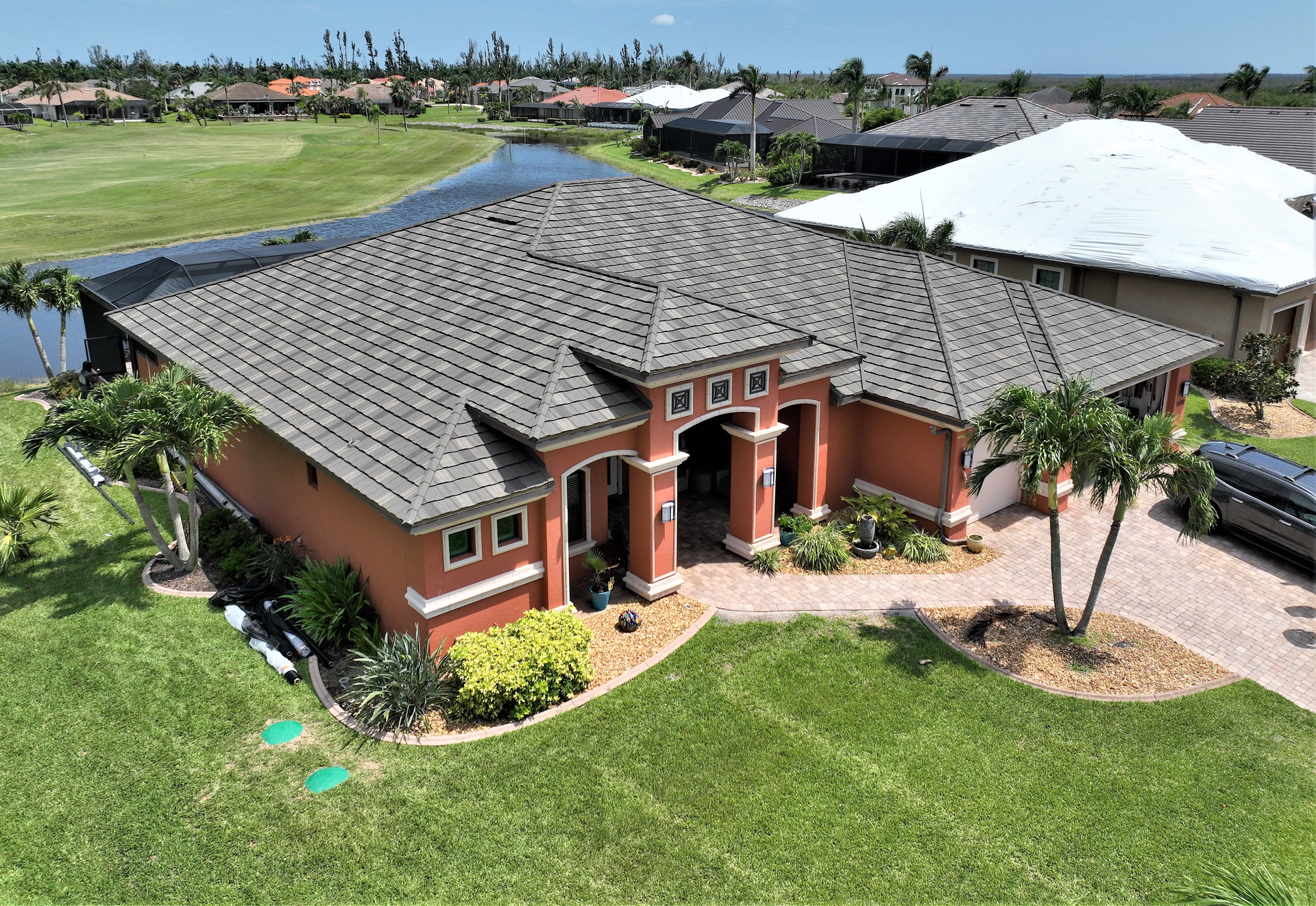 Orange stucco house with a dark gray tiled roof, a green lawn, and palm trees in a sunny setting.
