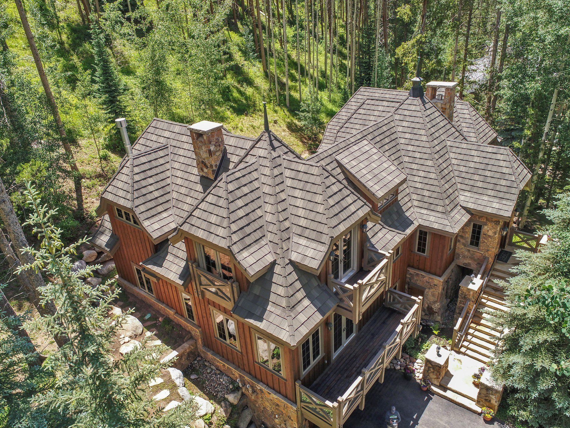 Aerial view of a large rustic house with a stone and wood exterior, nestled in a green forest setting.