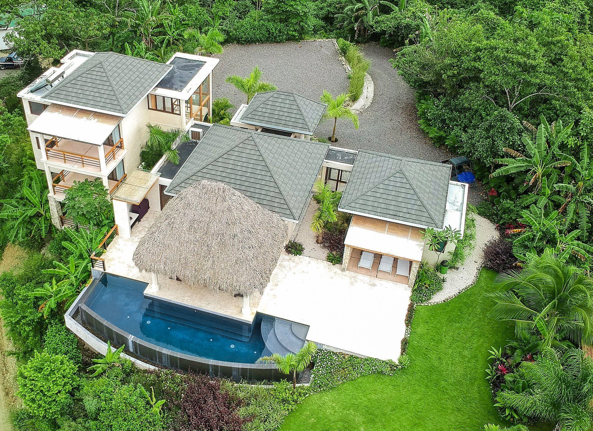 Aerial view of a luxurious home with a pool, surrounded by lush green vegetation.