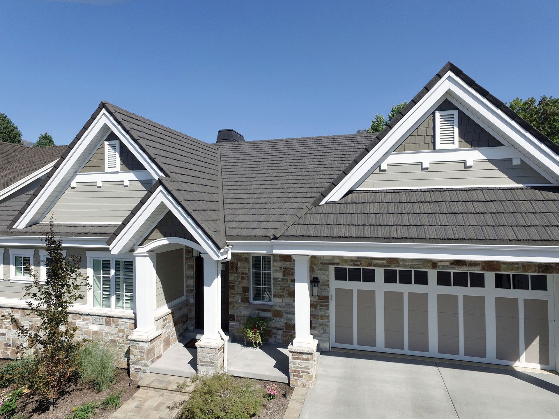 House exterior with gray roof, stone and light-colored siding, and a garage door. Clear blue sky overhead.