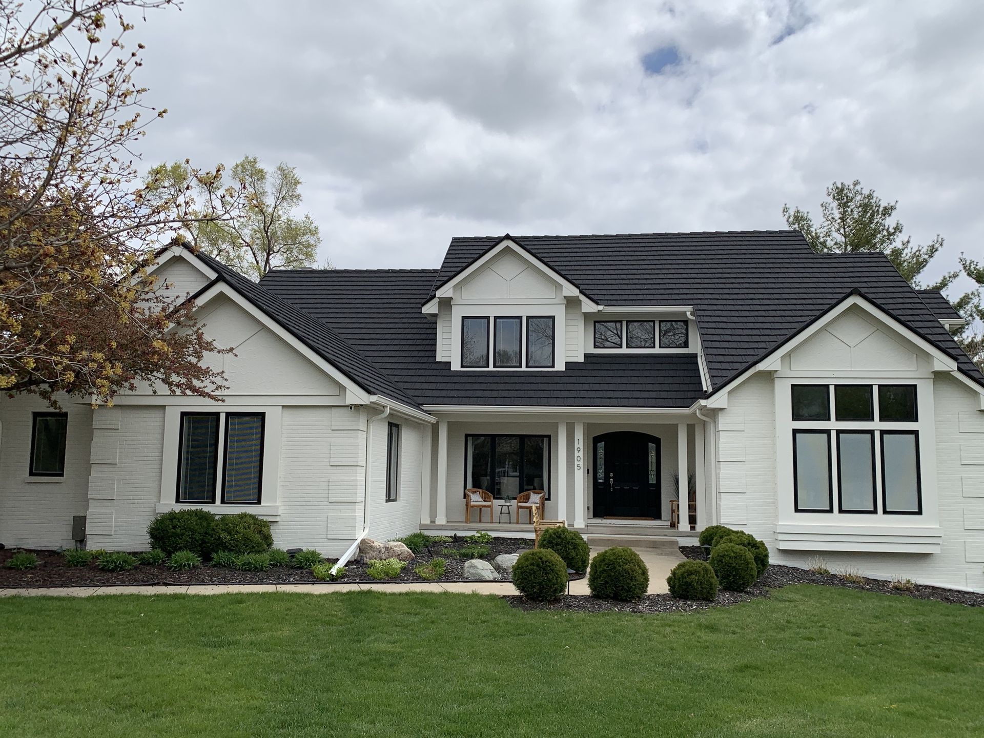 White house with a dark roof, black-framed windows, and a green lawn under a cloudy sky.