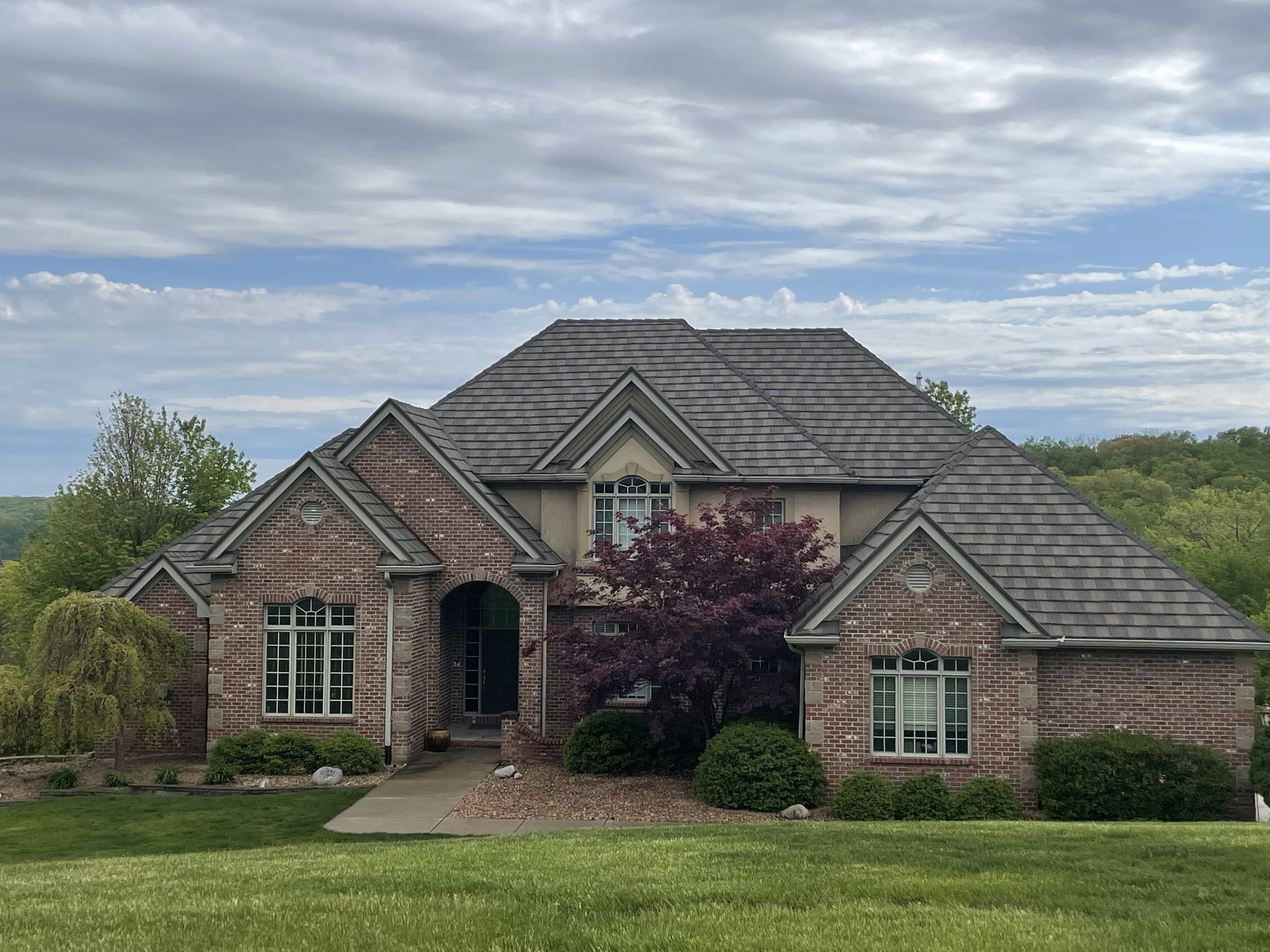Brick house with brown roof, tan trim, and manicured lawn against a cloudy sky.