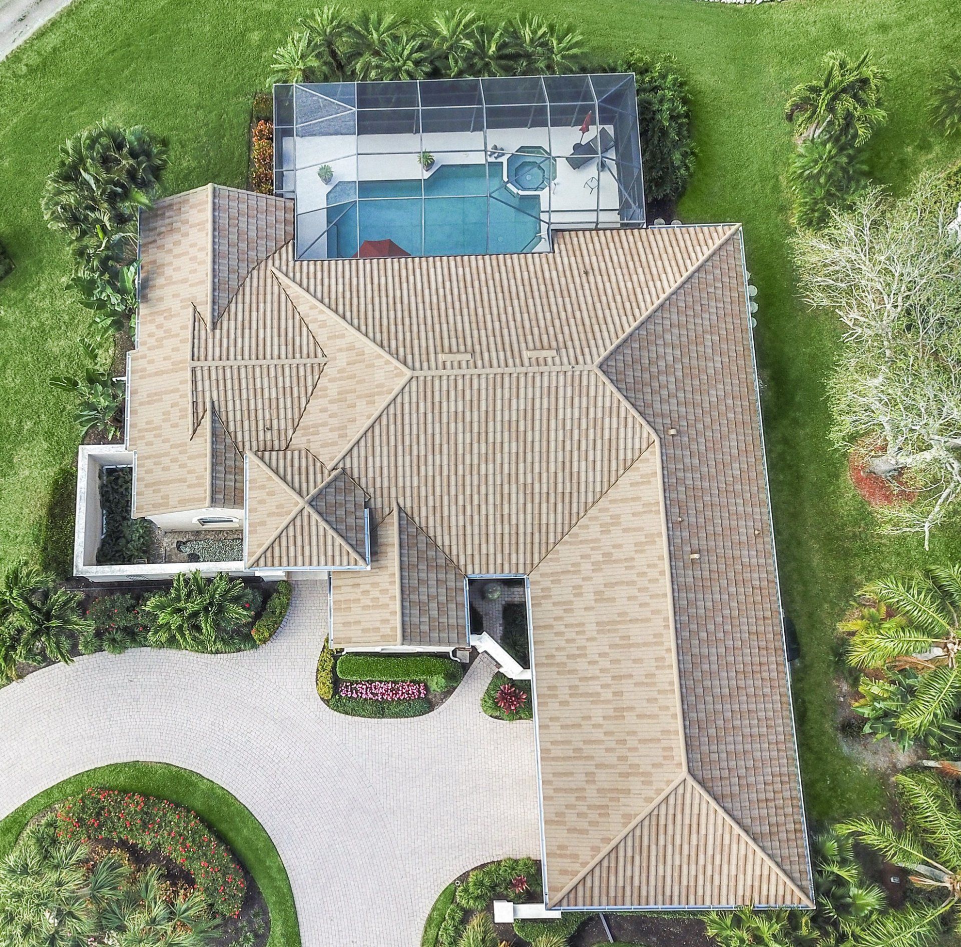Aerial view of a house with a pool in the backyard, a curved driveway, and lush green landscaping. The roof is brown.