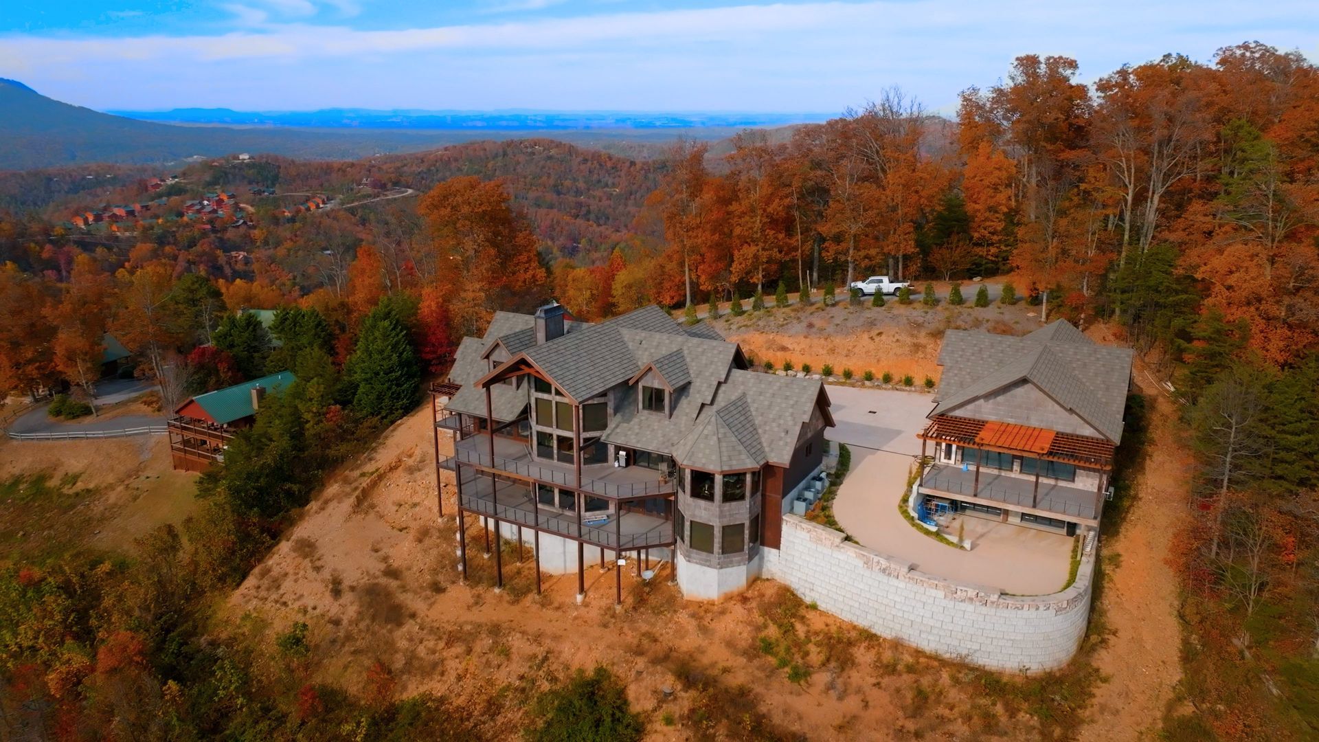 A large mountain home with a connected guest house, surrounded by fall foliage and overlooking a vast valley.