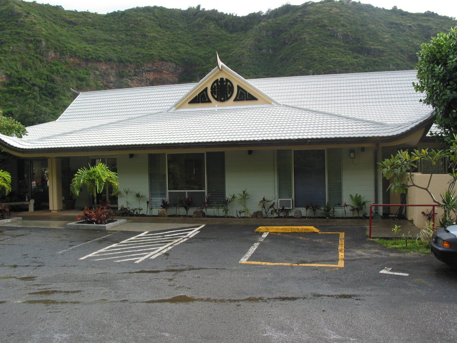 A one-story building with a light green exterior, white roof, and mountain backdrop; parking lot in foreground.