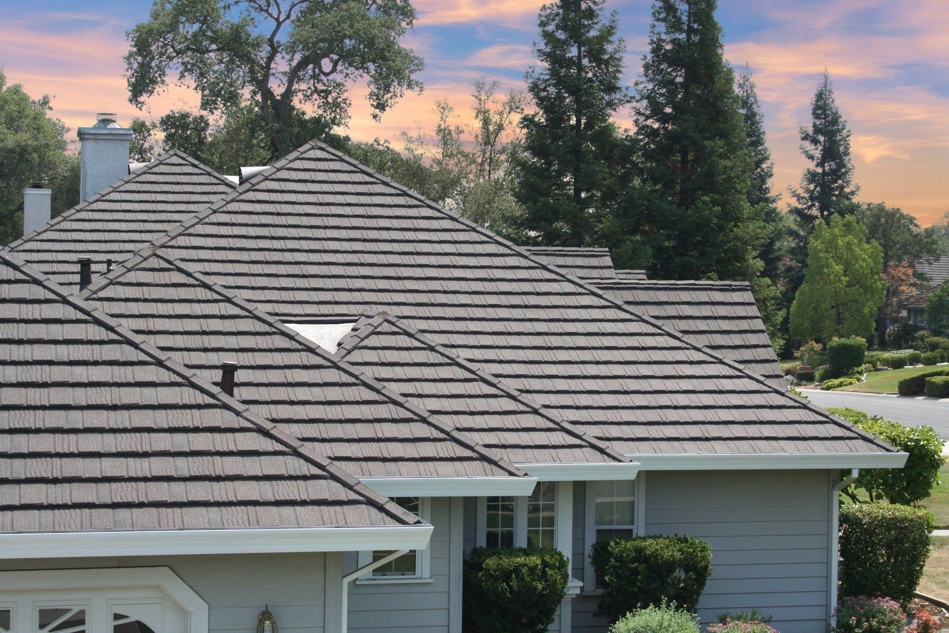 Gray roof of a house with a mix of trees and sky in the background.