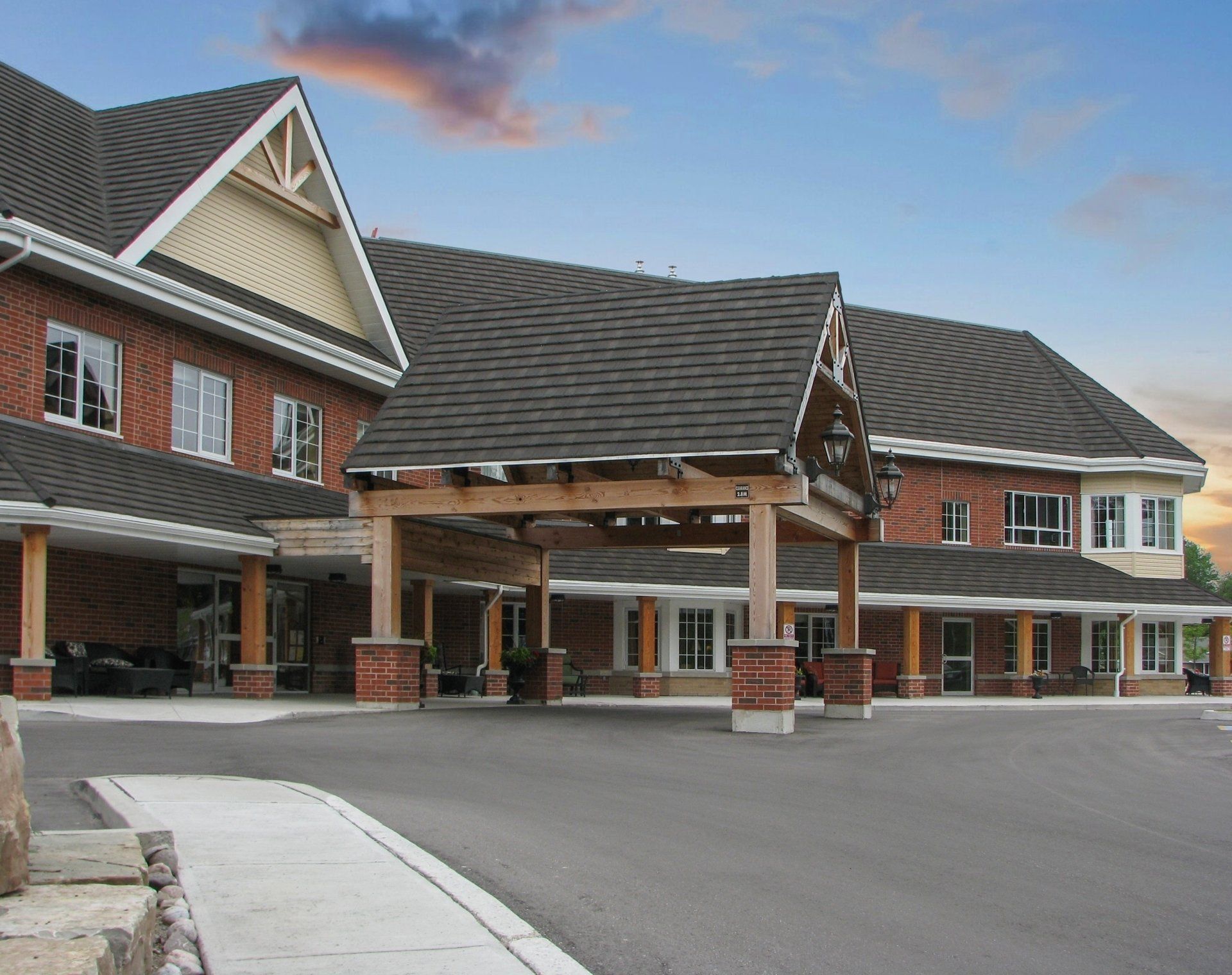 Red brick assisted living facility with a covered entrance. Dark roof, stone columns, and a paved driveway.