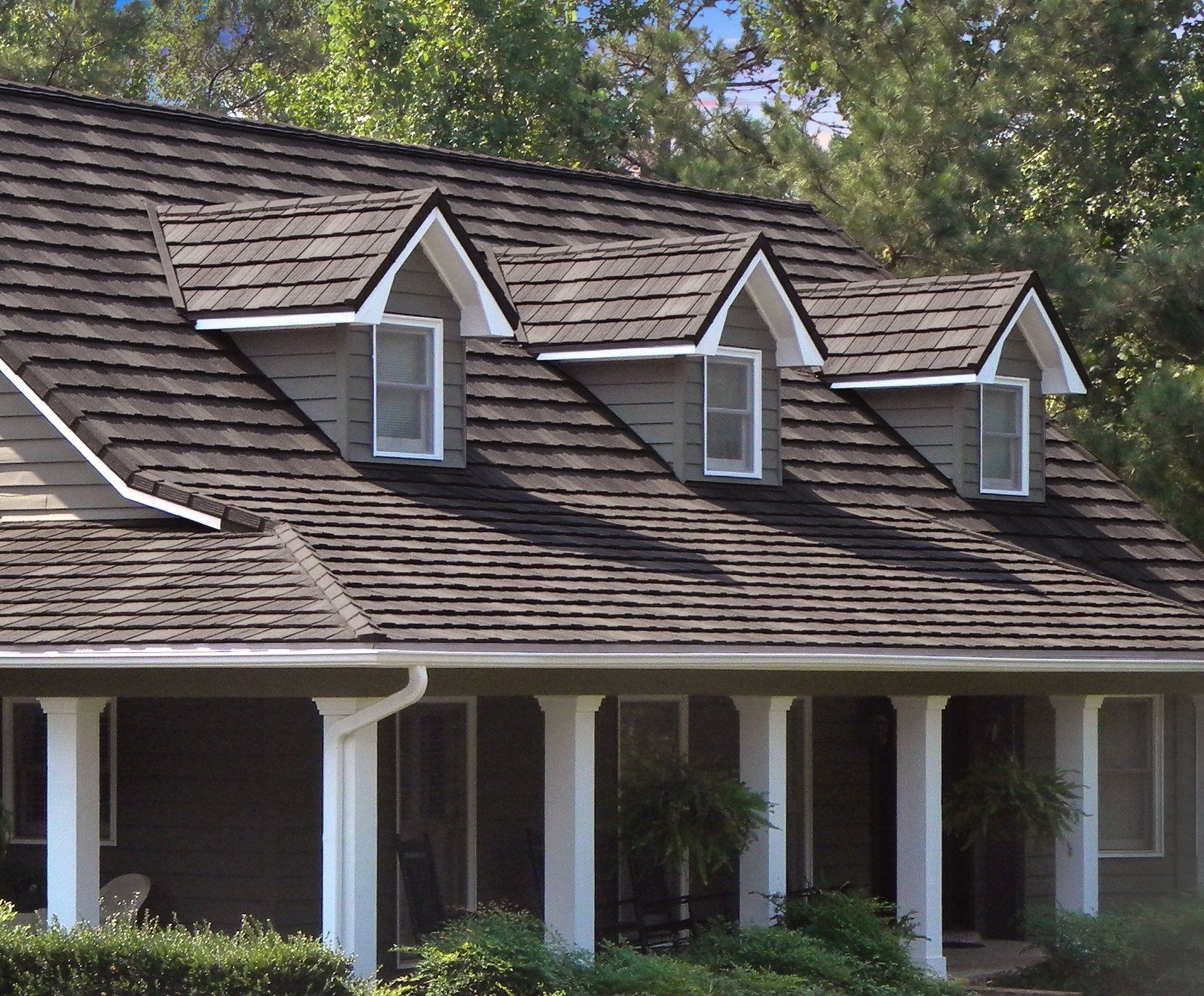 House with a dark roof, light-colored trim, and three dormers, set in a green, wooded area.
