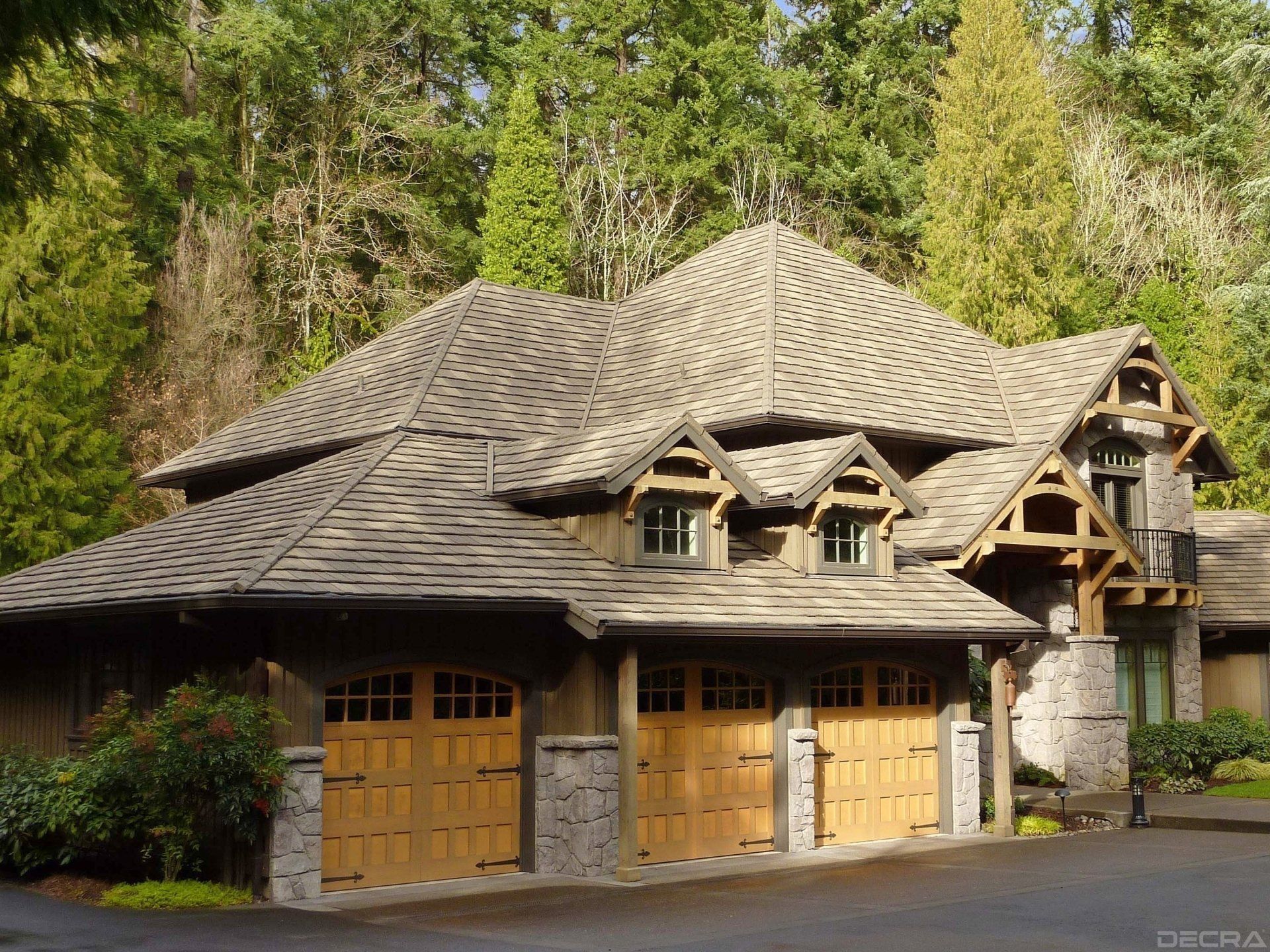 A rustic, two-story house with a stone and wood exterior, cedar-shake roof, and three-car garage. Set in a lush, wooded area.