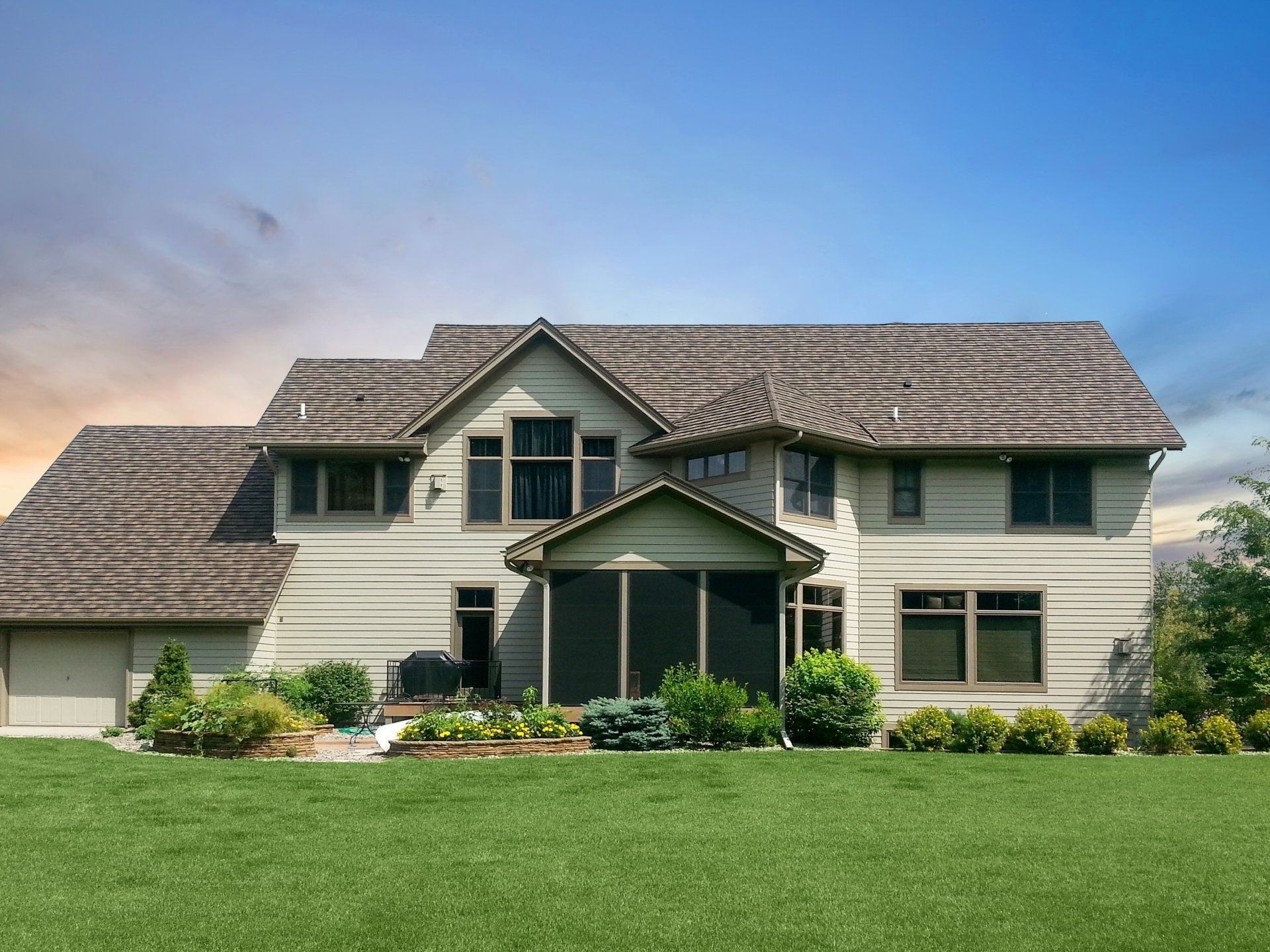 Two-story beige house with a gray shingle roof, a screened-in porch, and a green lawn under a blue and orange sky.