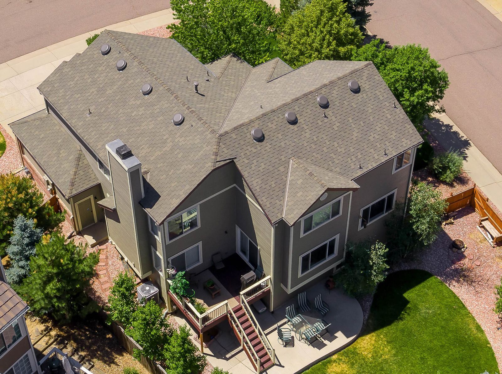Aerial view of a two-story house with a gray roof, a deck, and a backyard with grass and trees.
