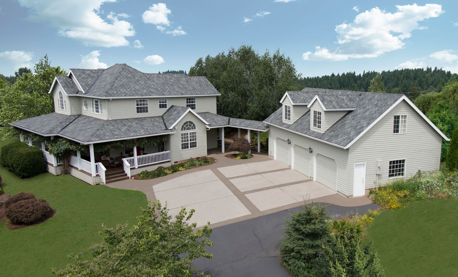 Large two-story house with attached garage, light siding, dark gray roof, and large paved driveway, set in a green yard.