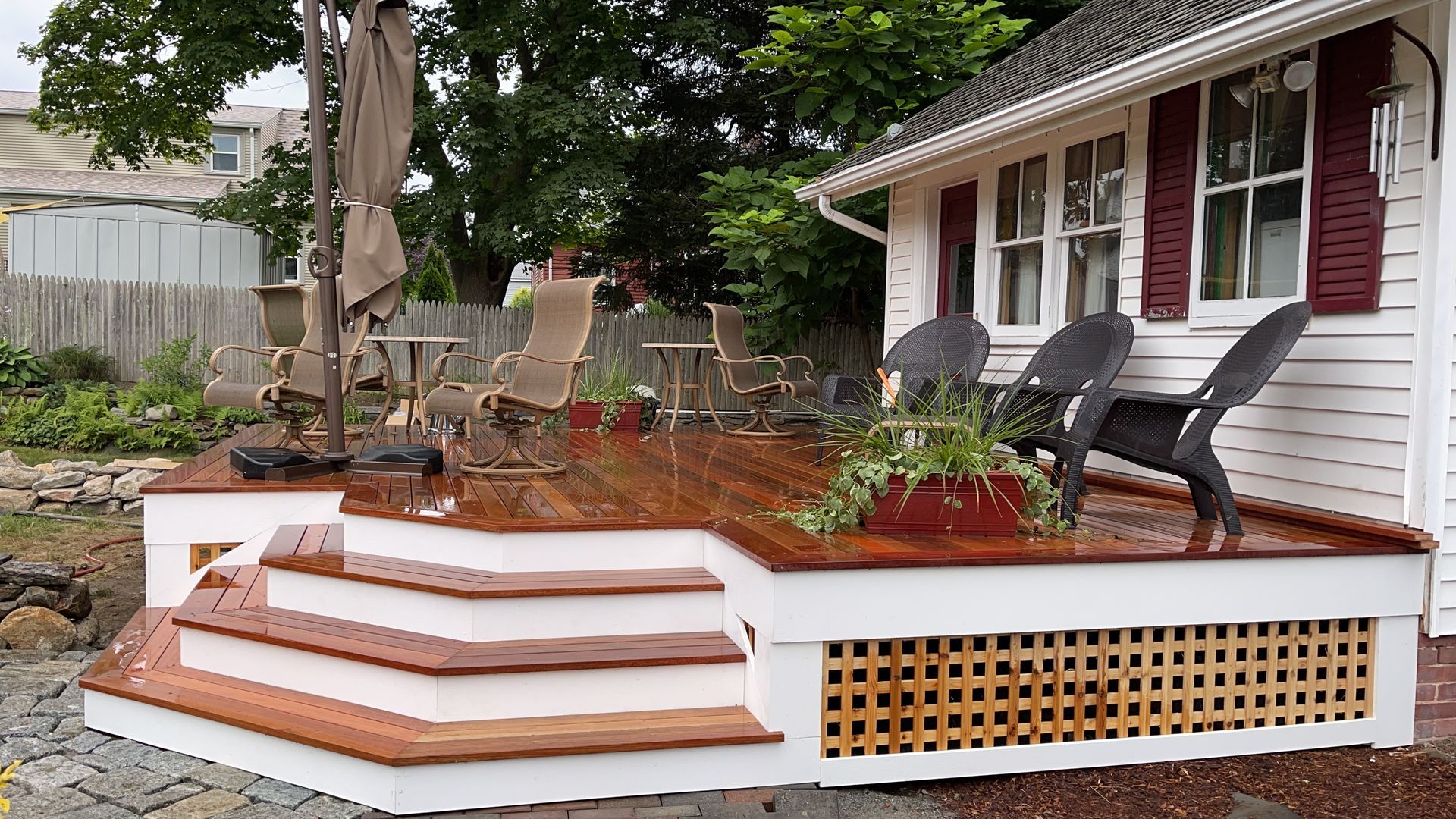 A wooden deck with chairs and umbrellas in front of a white house.