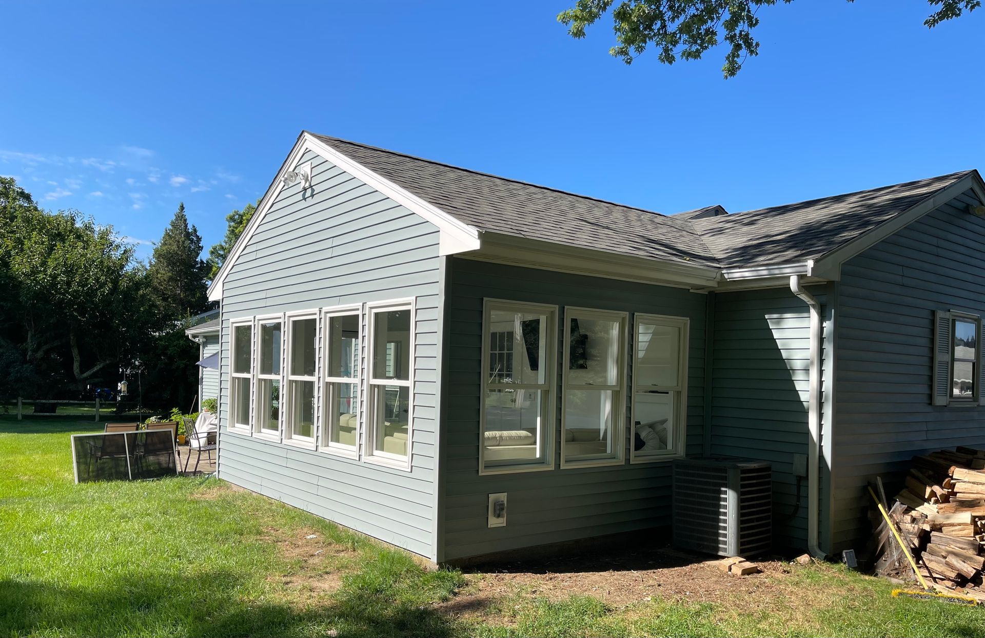 A house with a lot of windows is sitting on top of a lush green field.
