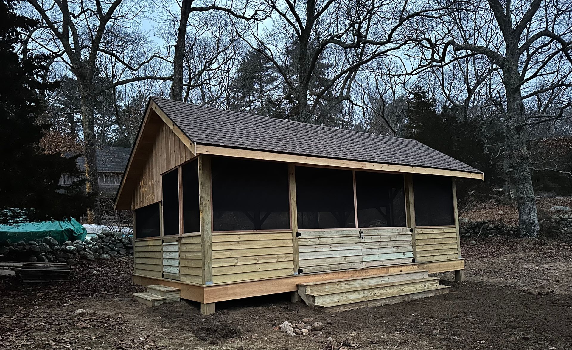 A small wooden house with a screened-in porch in the woods.
