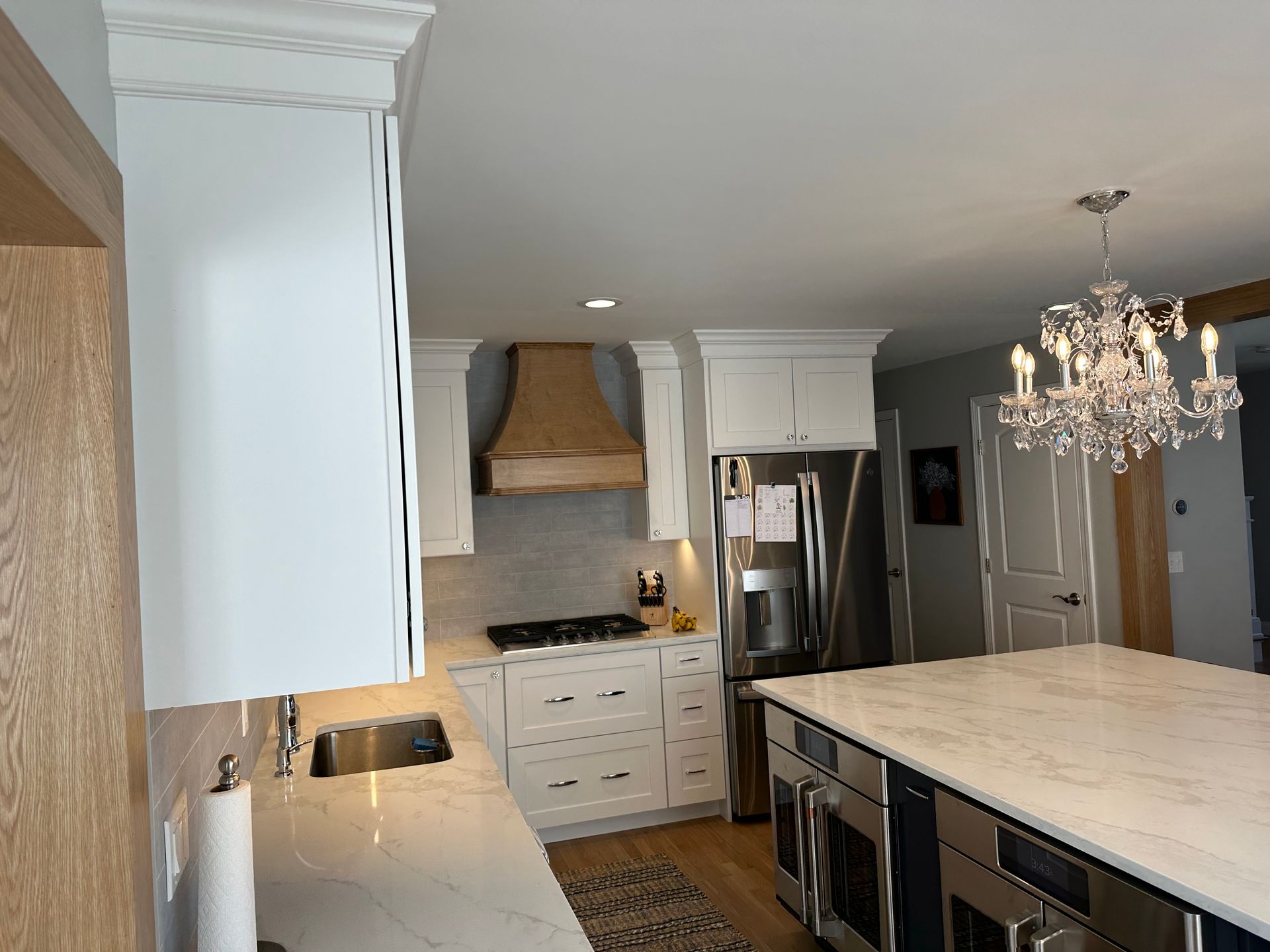 A kitchen with white cabinets and stainless steel appliances and a large island with a chandelier hanging from the ceiling.