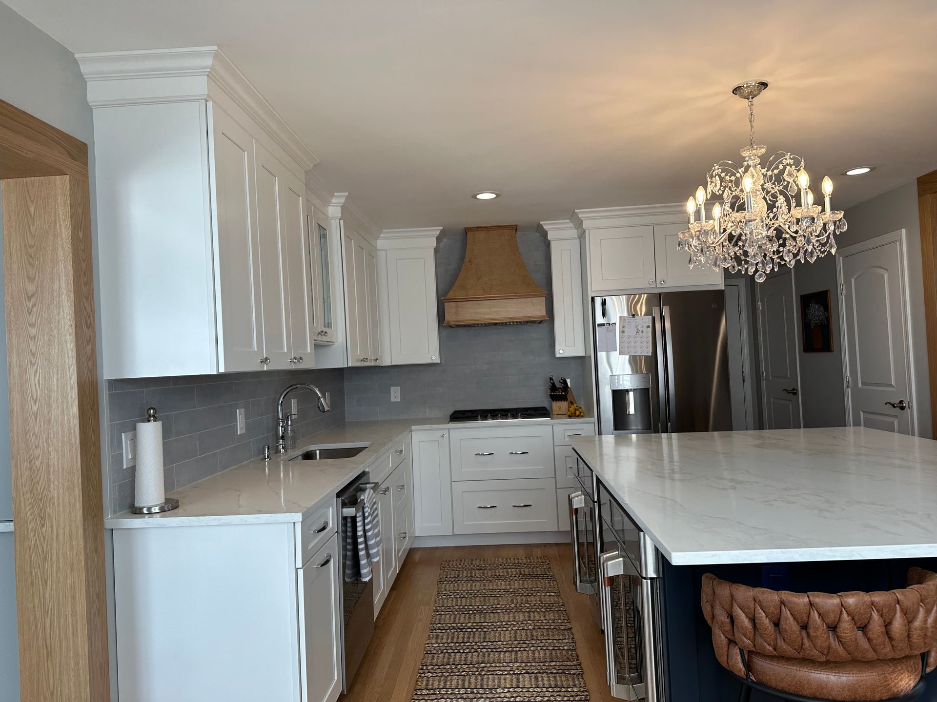 A kitchen with white cabinets, stainless steel appliances, a large island, and a chandelier.