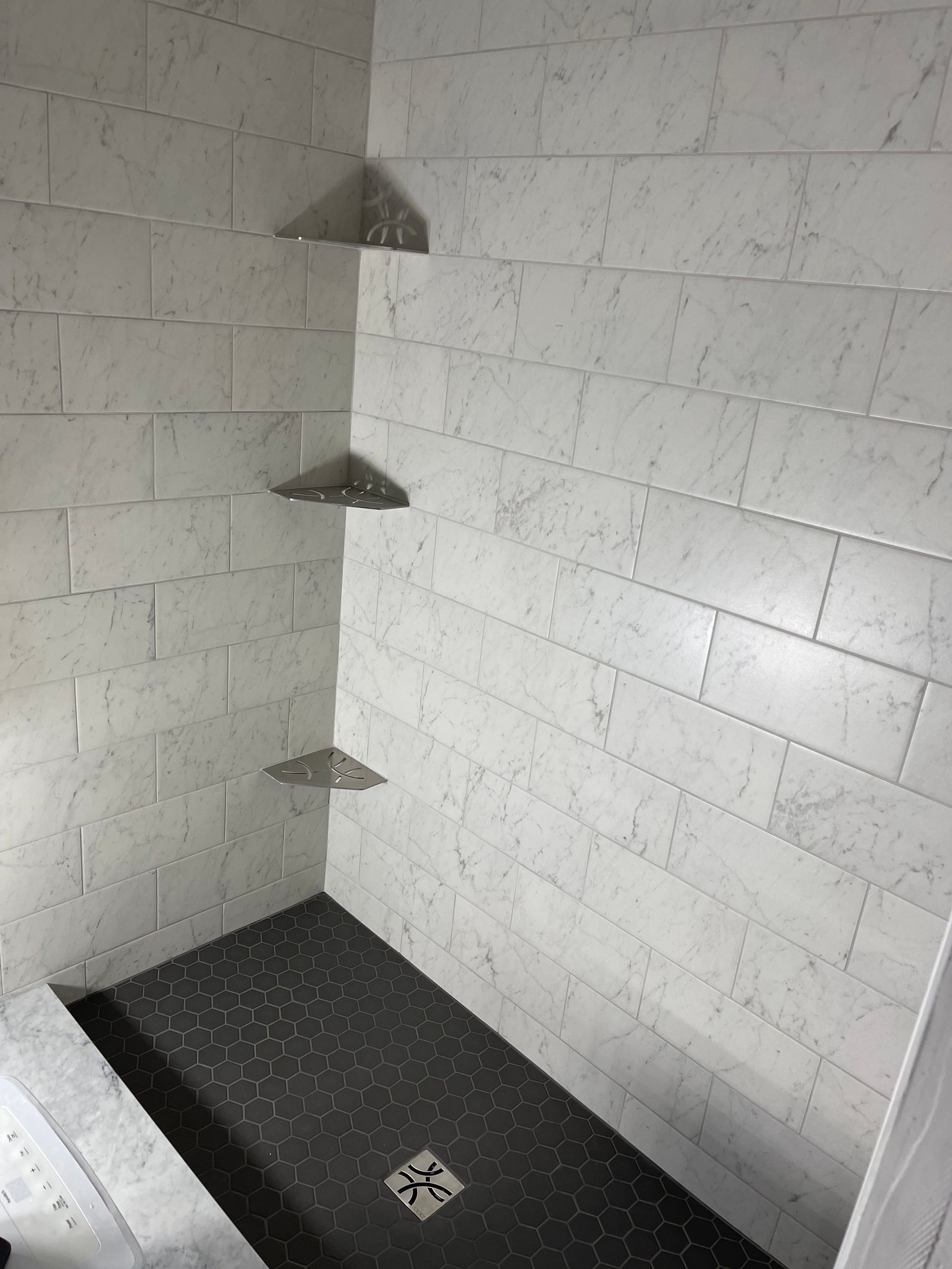 A shower stall with white tiles and a black floor.