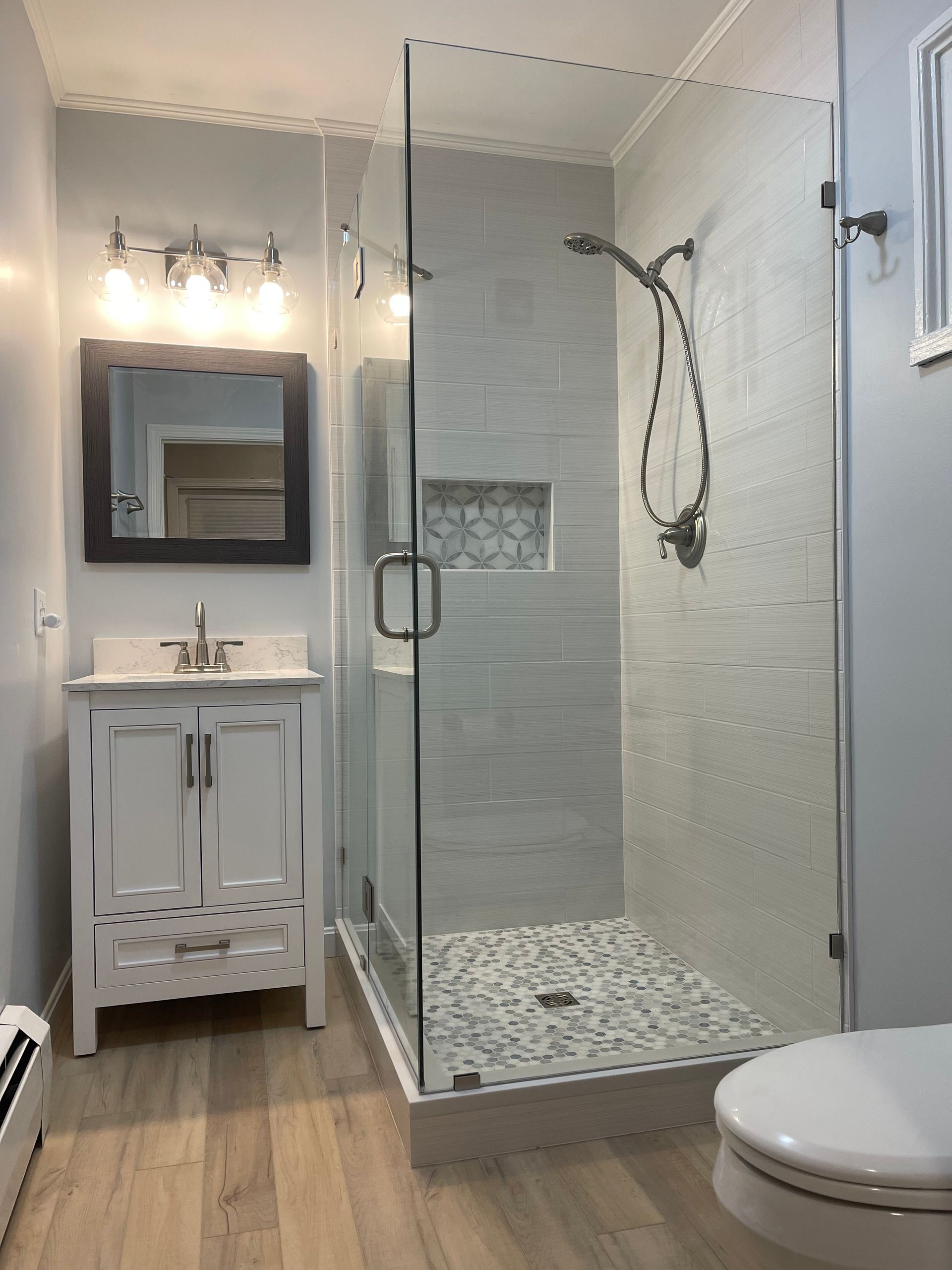 A bathroom with a walk-in shower, sink, toilet, and mirror.