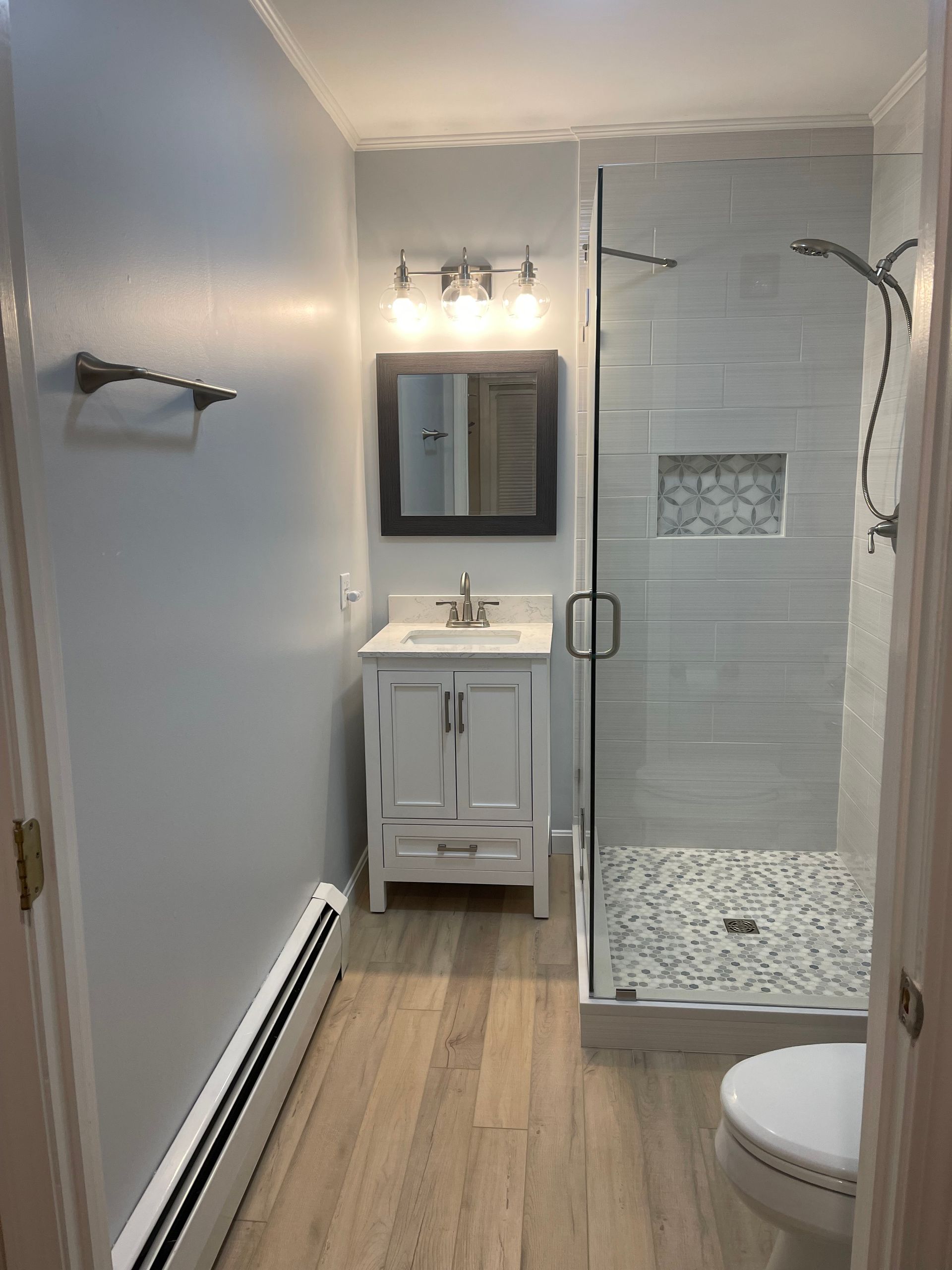 A bathroom with a sink, toilet, shower and mirror.