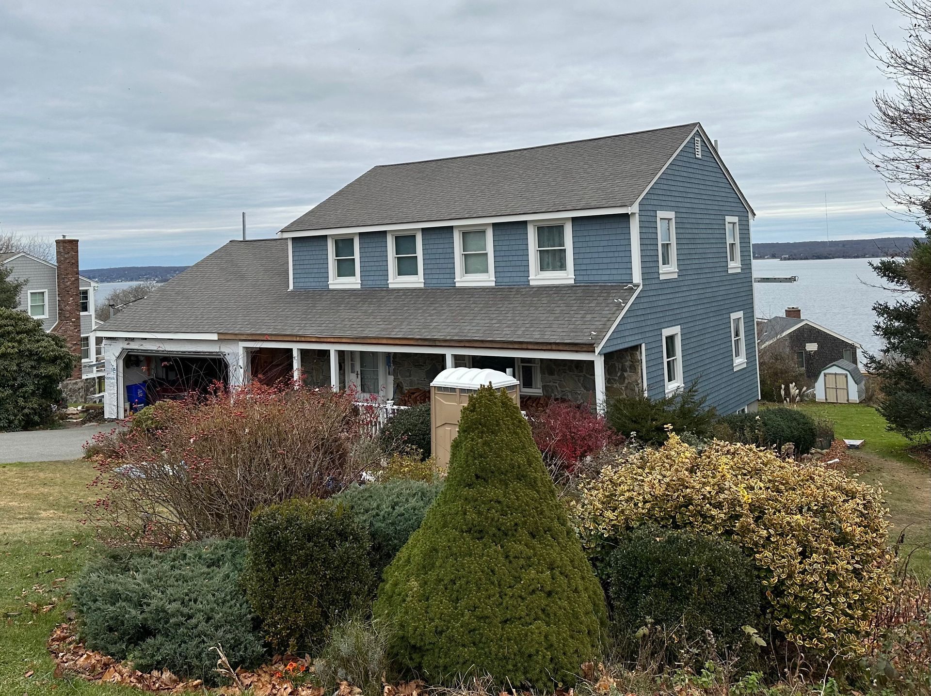 A large blue house with a gray roof is surrounded by bushes and trees.
