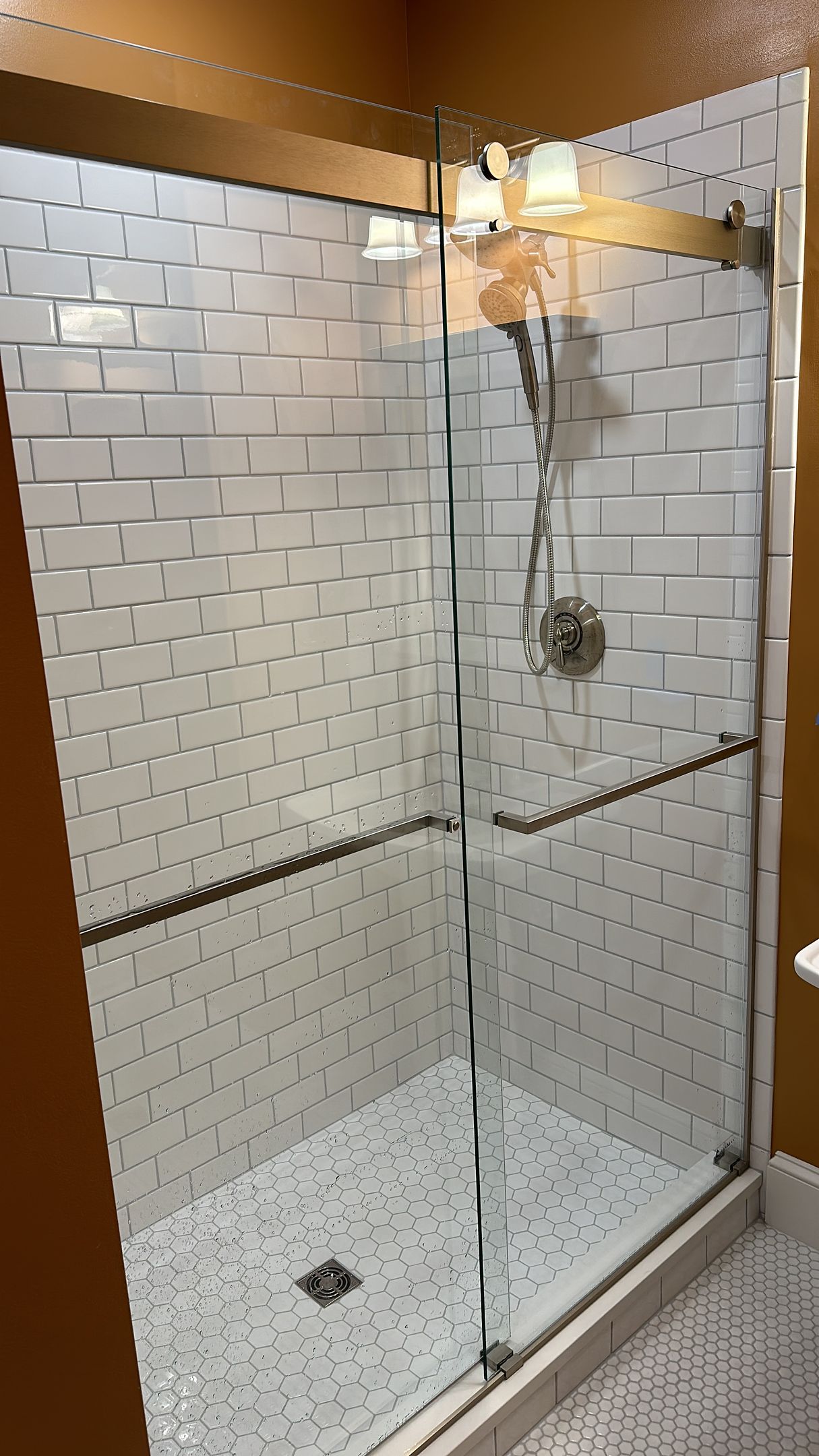 A shower with a glass door and white tiles on the wall.
