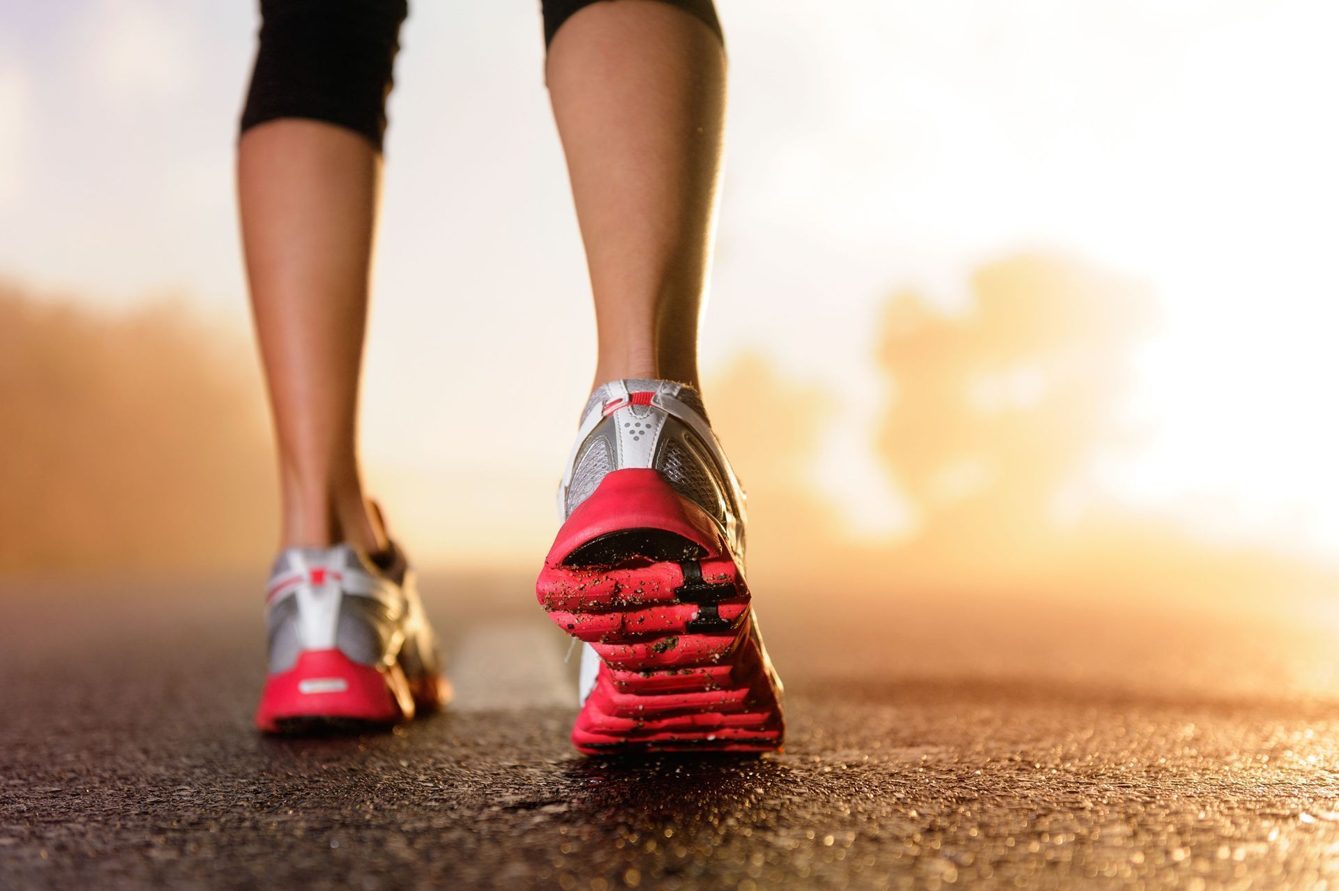 Person walking on a wet road at sunrise, wearing running shoes.