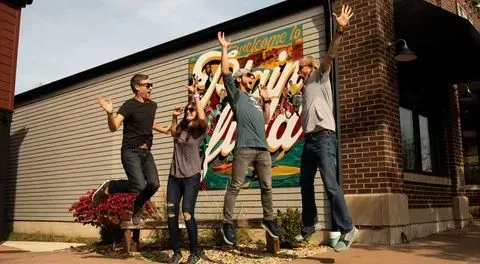 Five people jumping with arms raised in front of a building with a large sign.