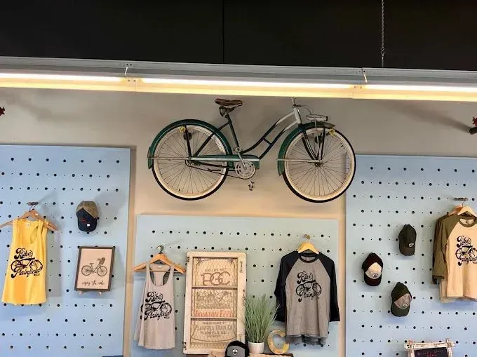 Bike shop display featuring a mounted bicycle above clothing racks with bike-themed apparel.