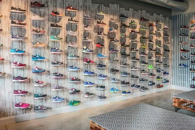 Wall display of colorful sneakers on shelves in a retail store, with wooden plank background and seating.