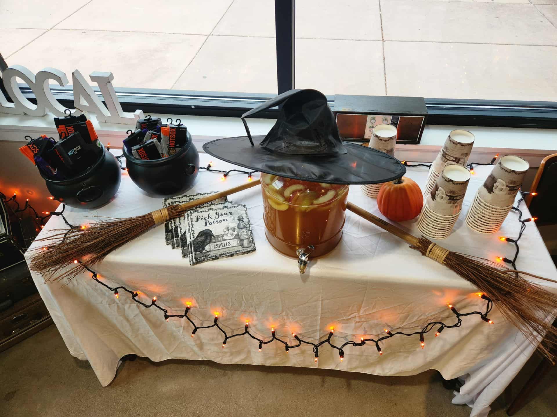 Halloween-themed drink station with a cauldron, witch hat, pumpkin, and orange string lights.