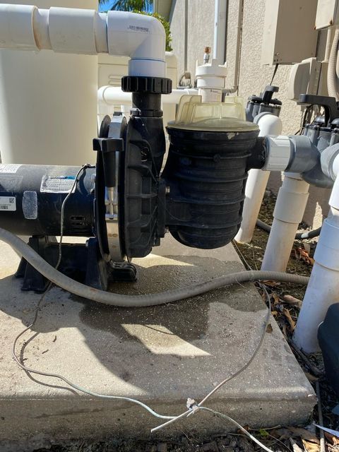 Pool pump system on concrete pad, with pipes, filter, and electrical wiring, in an outdoor setting.
