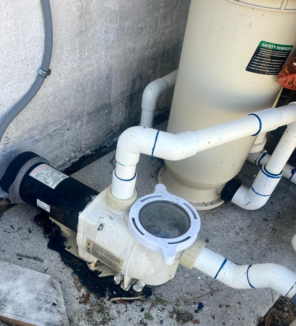 Pool pump leaking dark fluid on concrete near plumbing and filter.