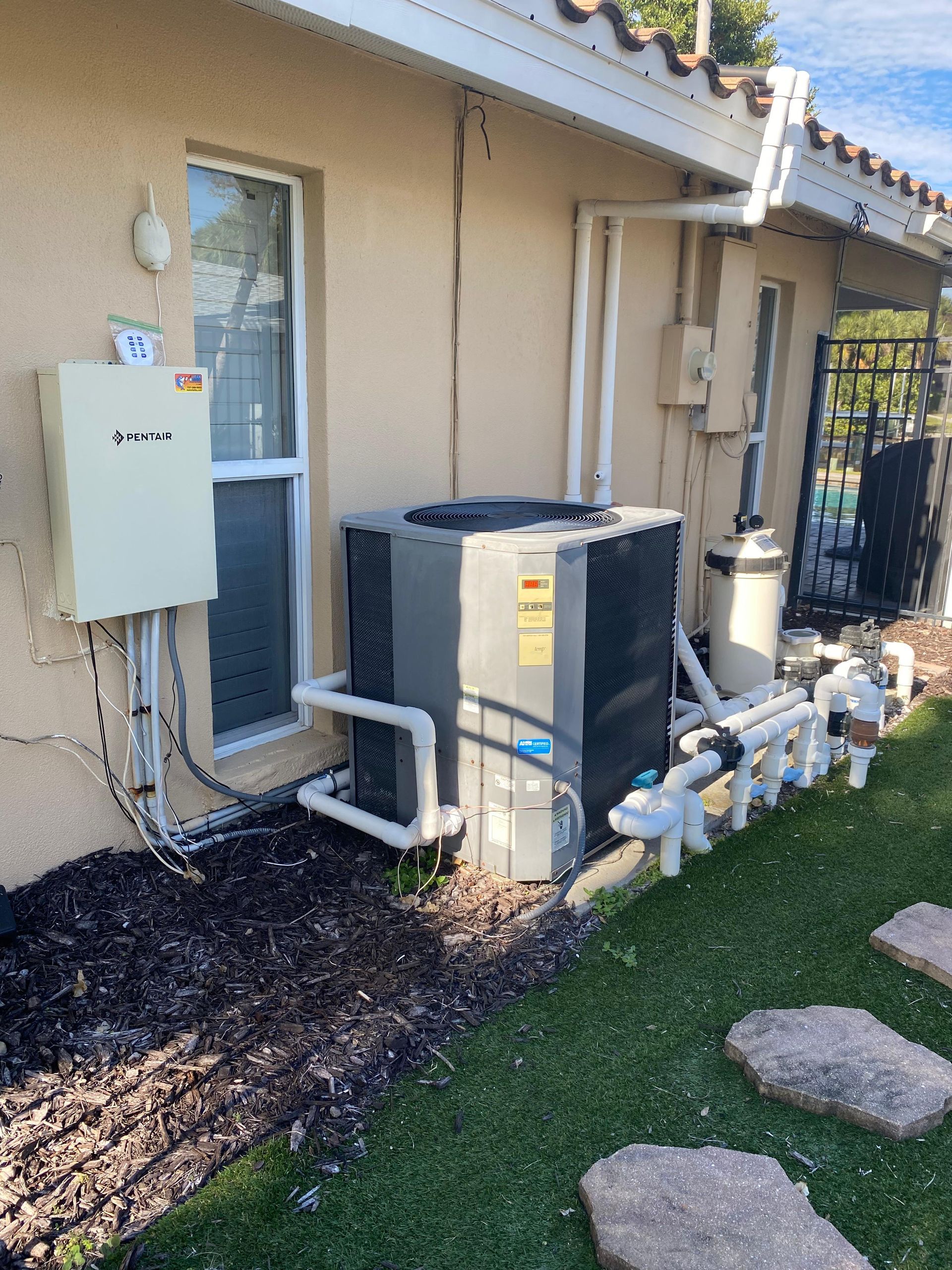 An outdoor HVAC unit next to a house with pool equipment on a grassy area.
