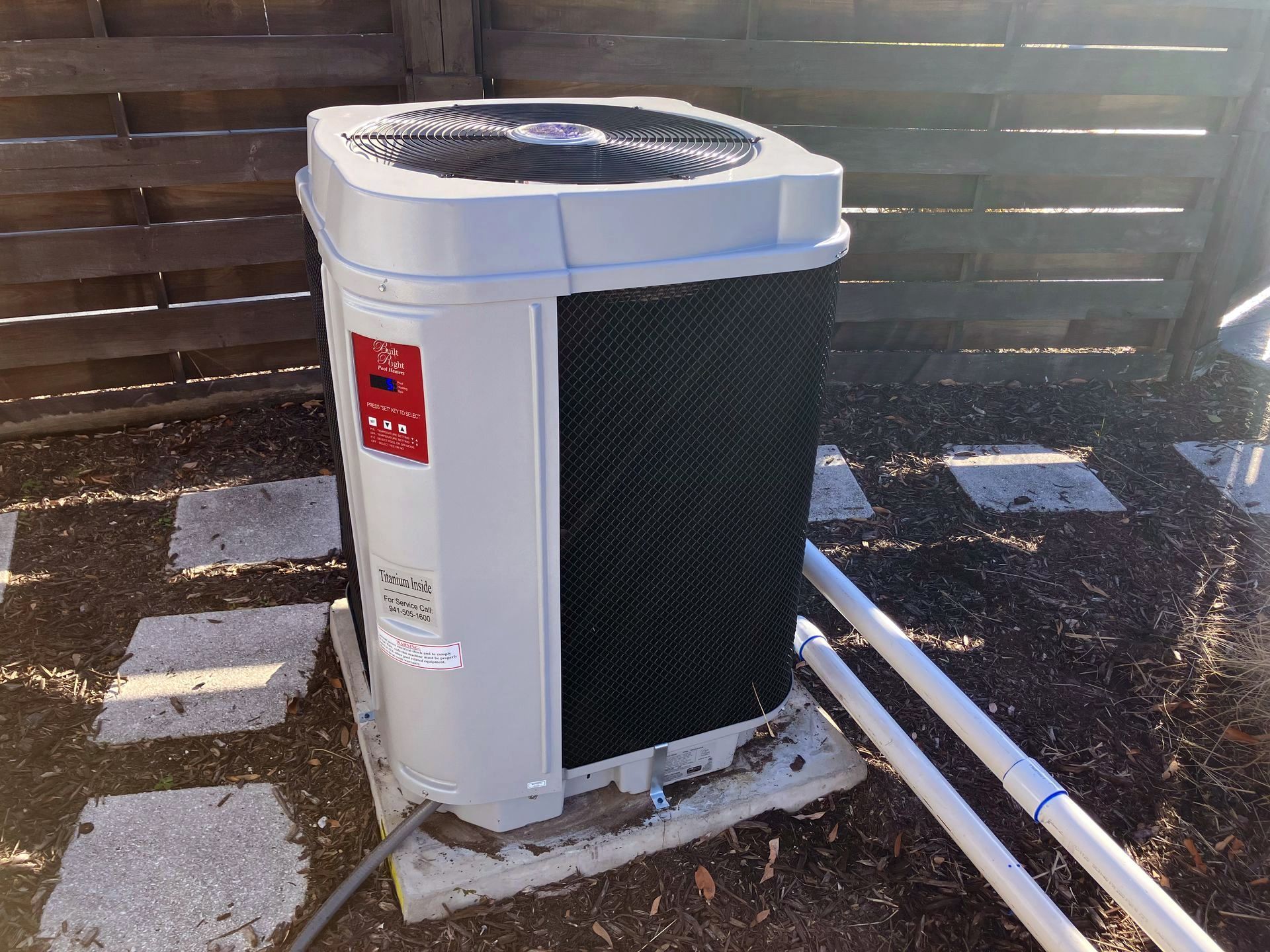 Outdoor heat pump unit on a concrete pad with exposed pipes.