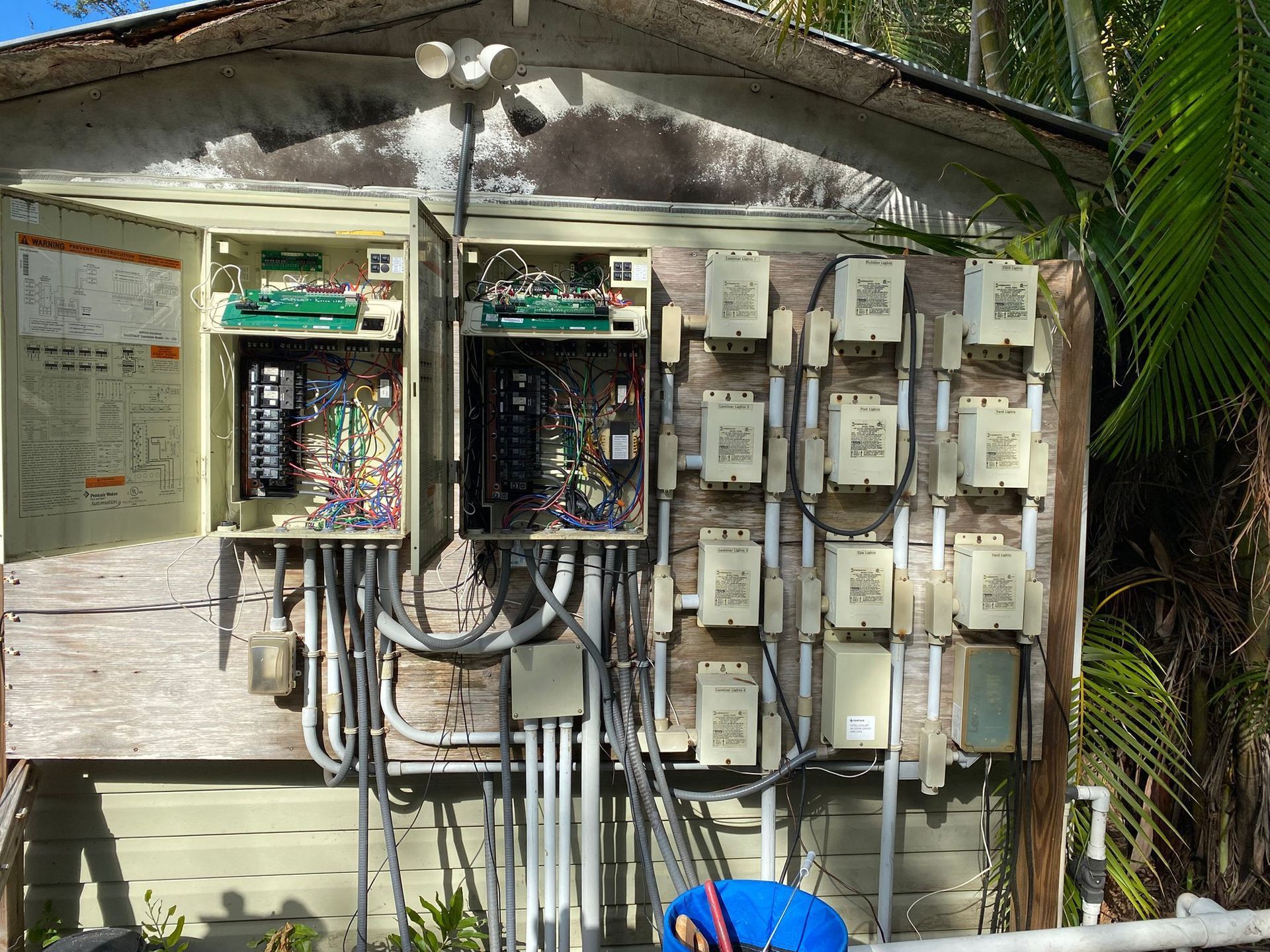 Electrical boxes and wiring mounted on a weathered building, outdoor setting.