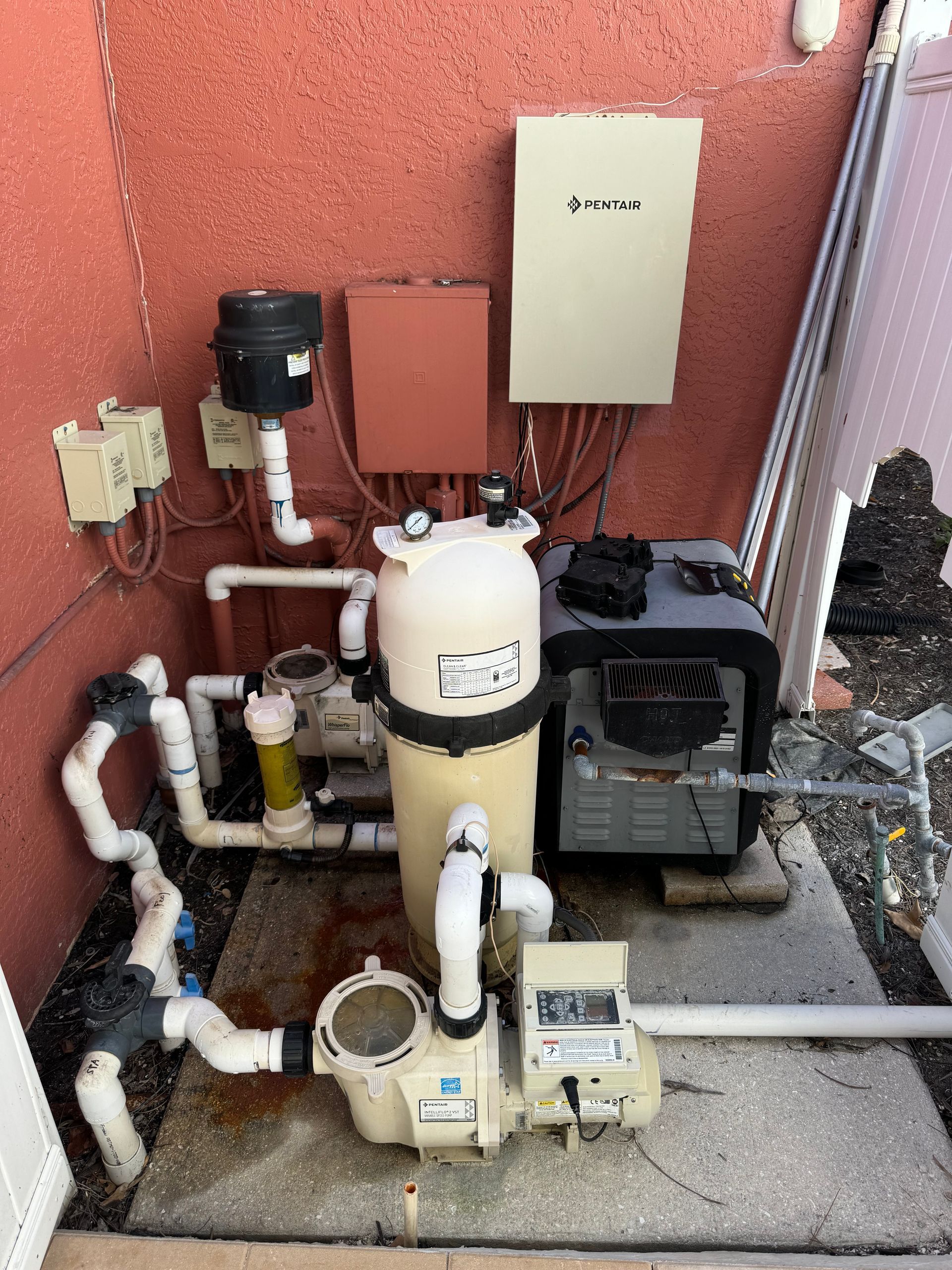 Pool equipment, including a pump, filter, heater, and electrical boxes, set against a stucco wall.