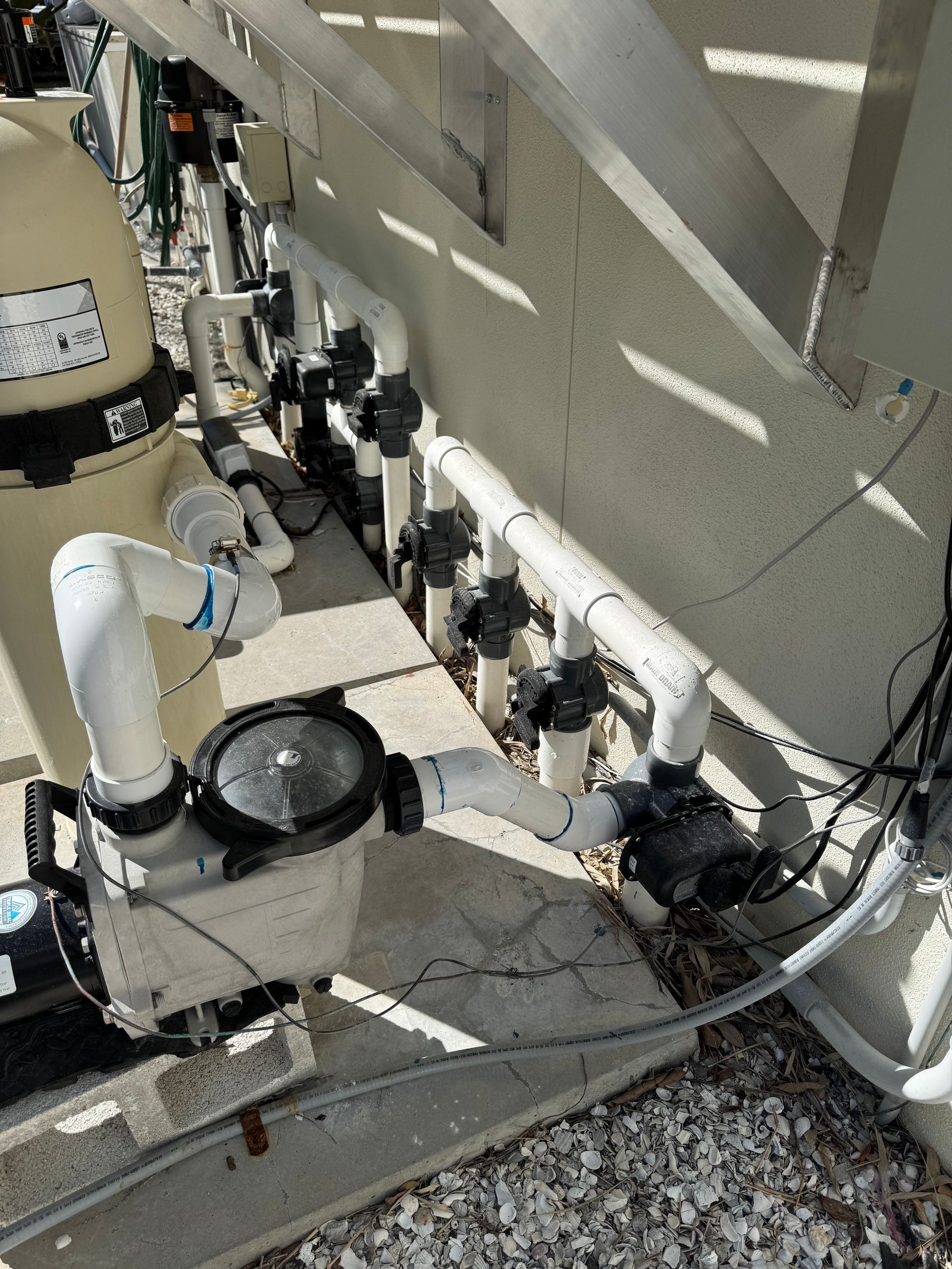 Pool equipment: filter, pump, and plumbing with valves installed outdoors near a wall.