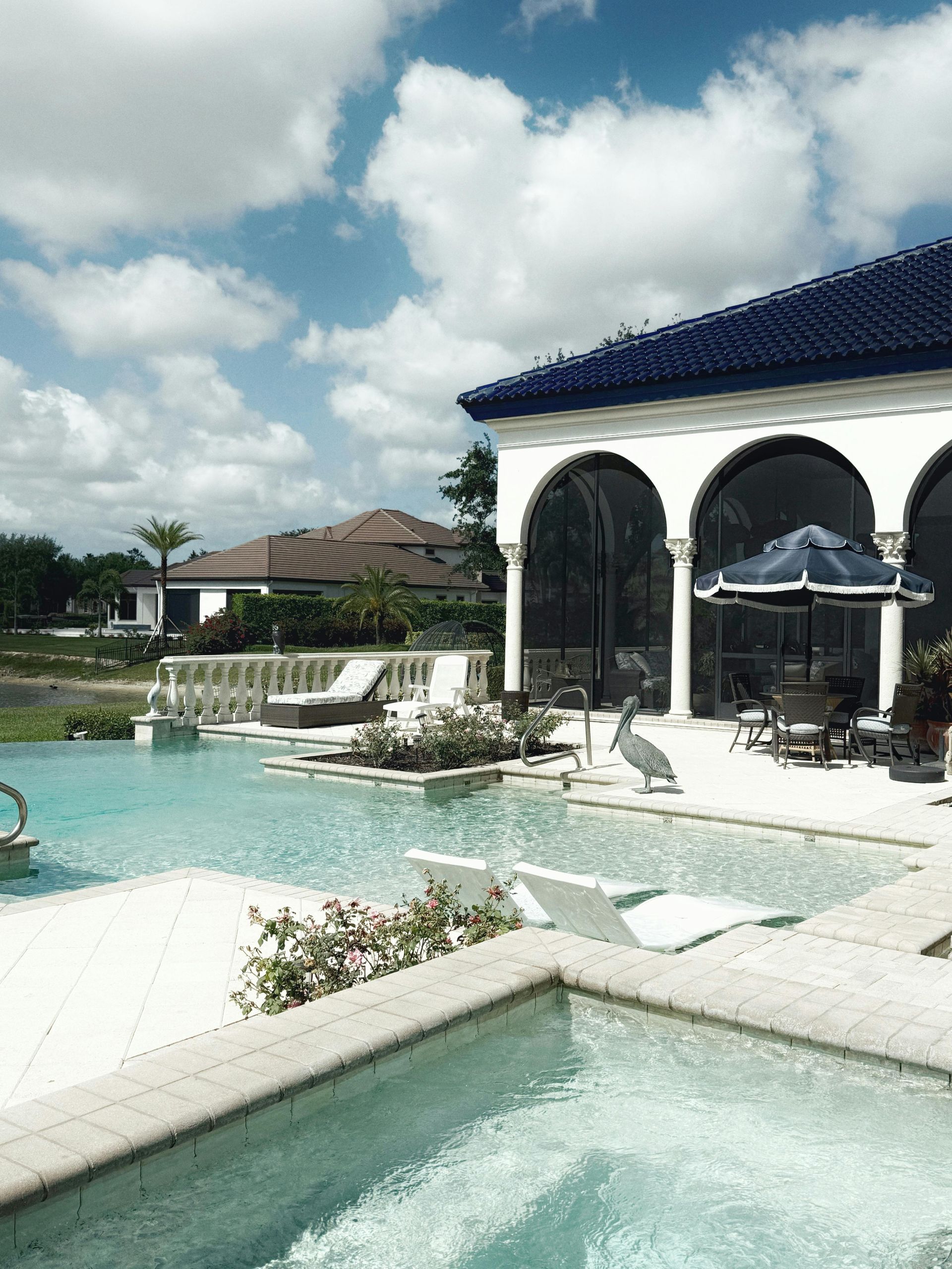 A luxury home with a blue-tiled roof, pool, and spa under a partly cloudy sky.