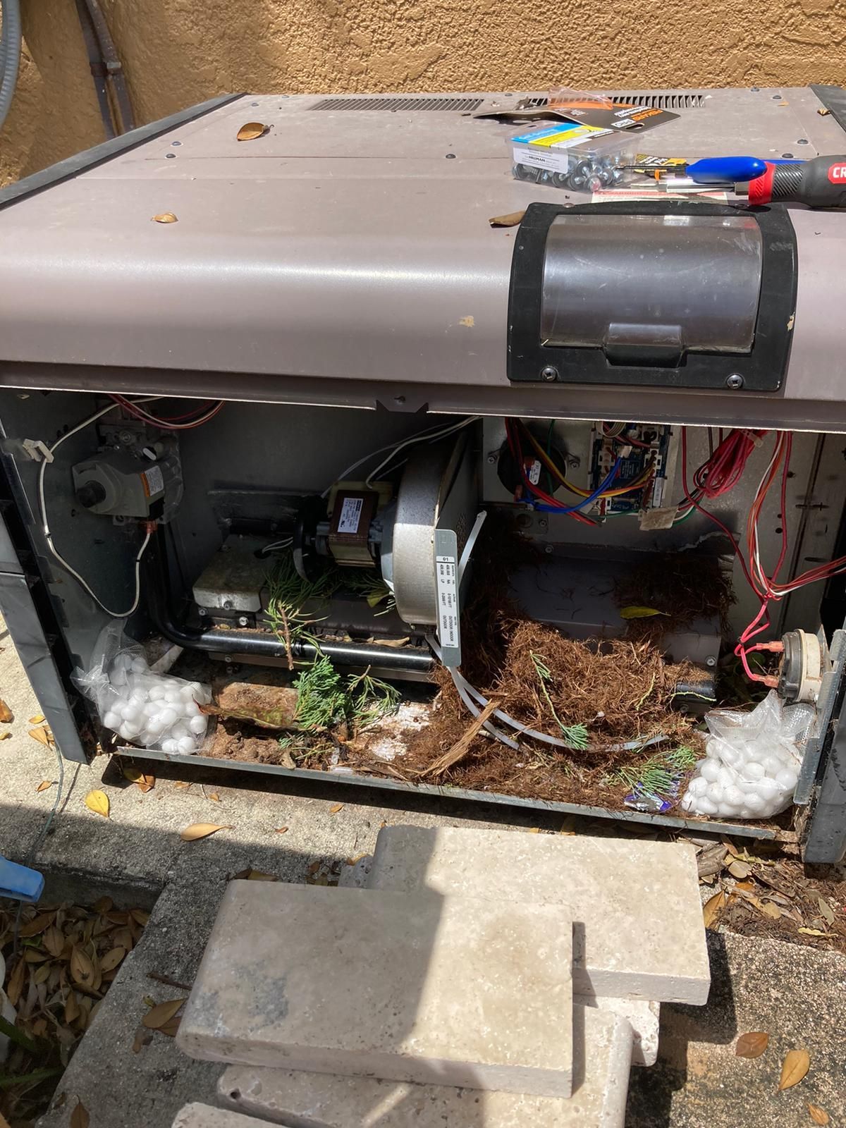 Open HVAC unit with debris inside; beige and gray exterior, concrete setting.