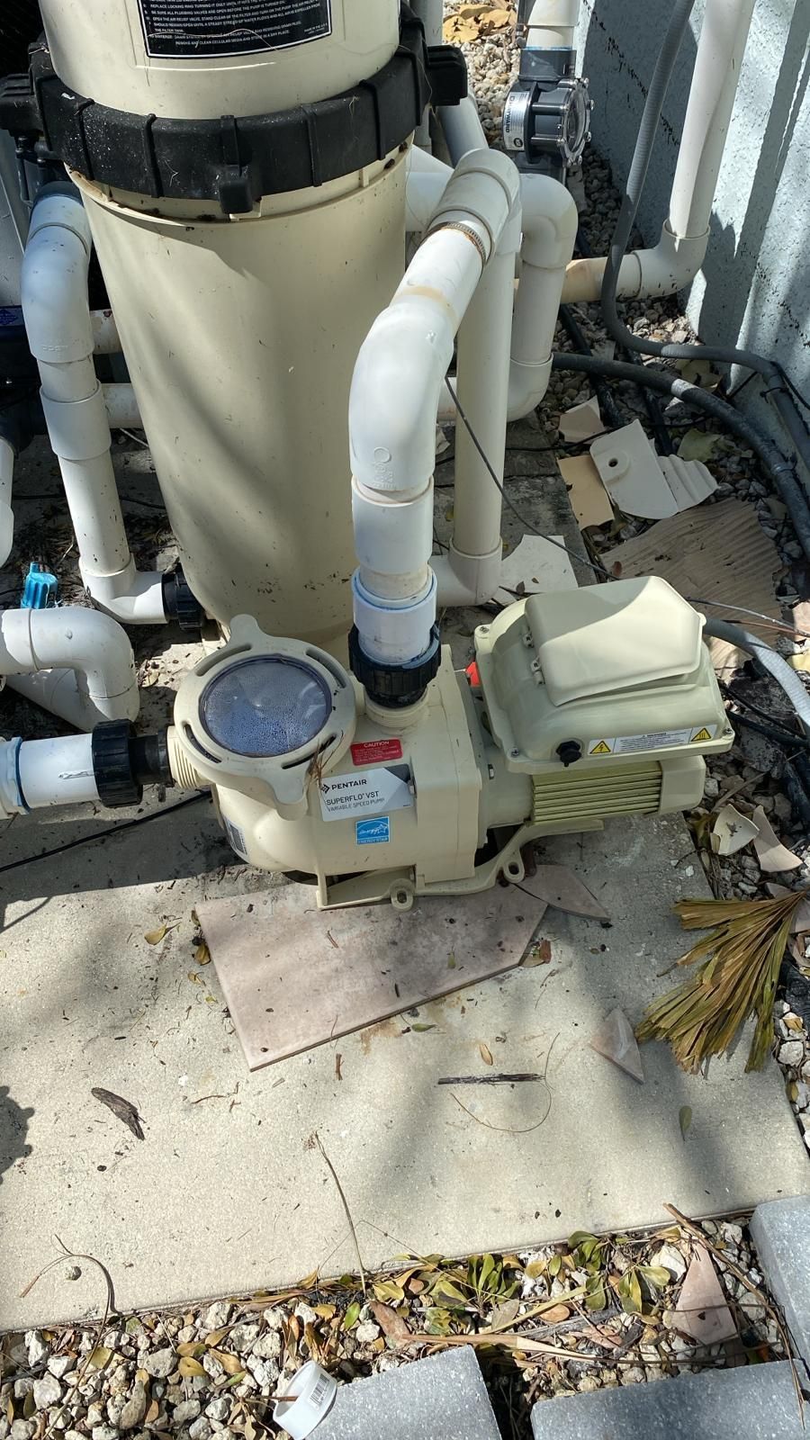 Pool pump and filter system; beige pump, white pipes, filter tank outdoors.