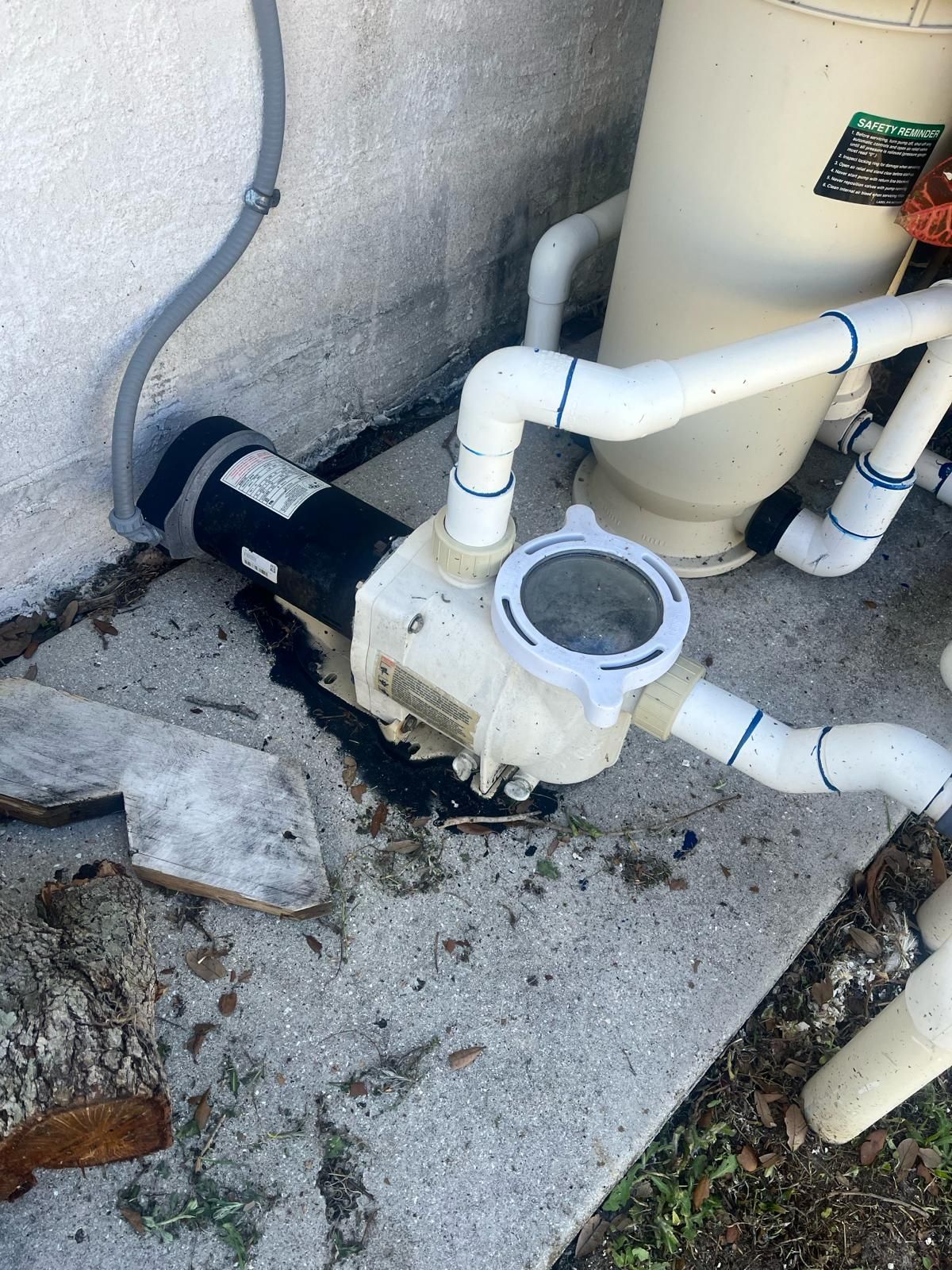 Pool pump with plumbing, filter, and wet concrete near a building.