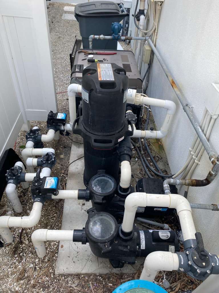 Pool equipment including pumps, filter, and plumbing in a narrow outdoor space.