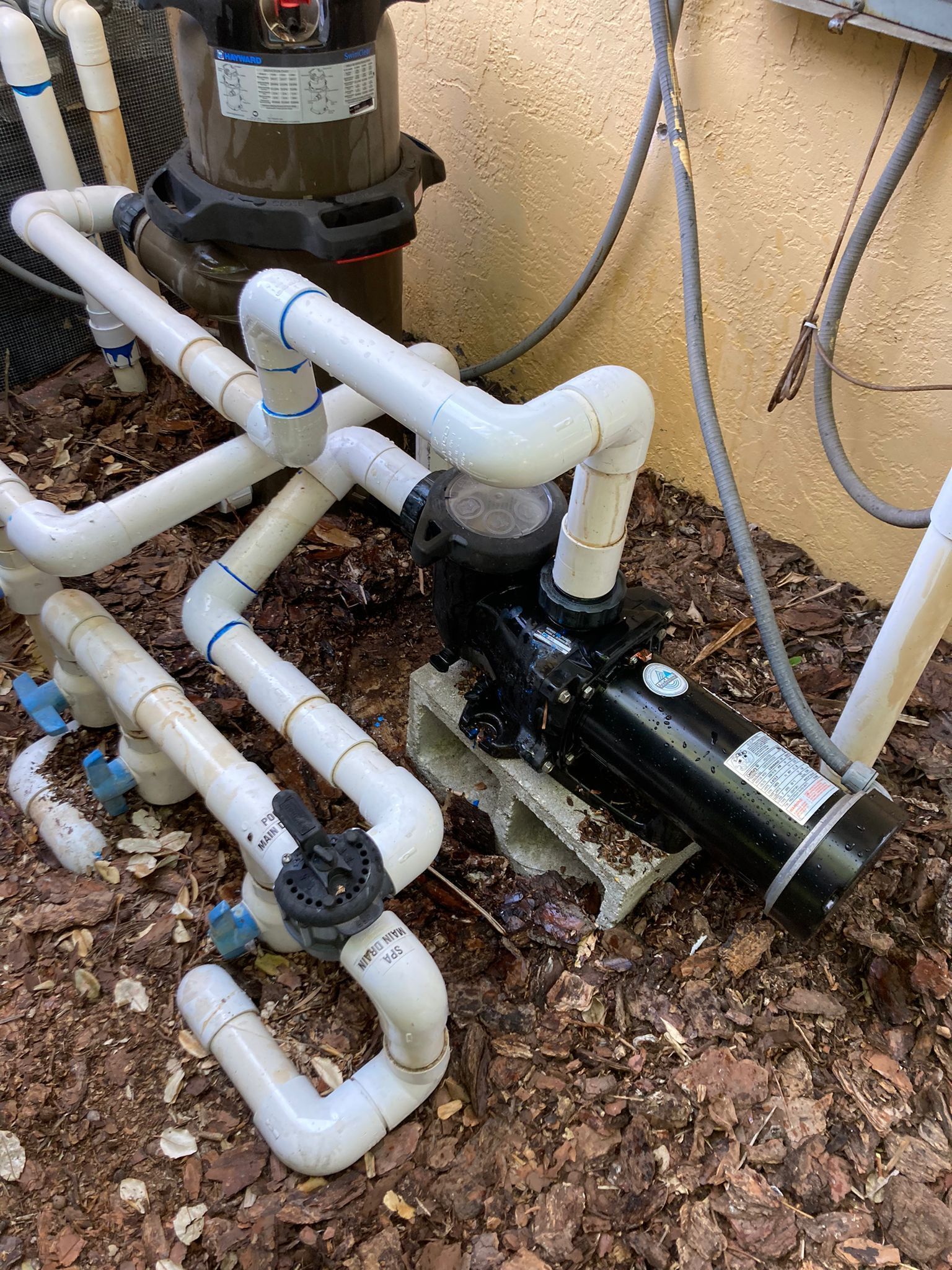 Pool pump system with white pipes and black pump on mulch.
