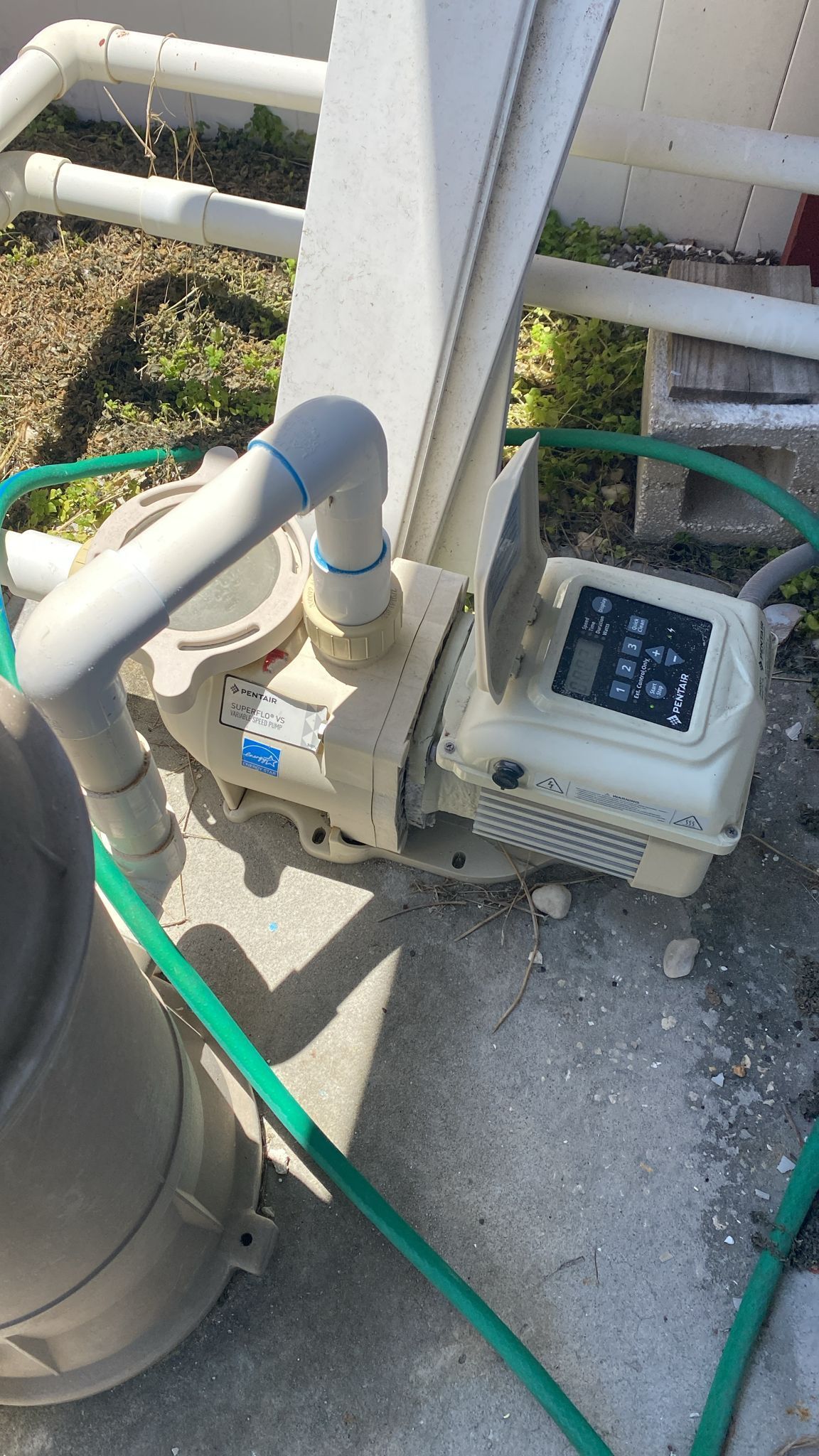 Tan pool pump with digital display, connected to pipes and hoses, outside.