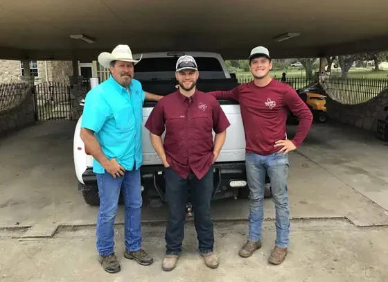 Three men standing in front of a white truck. One wears a cowboy hat, another a cap. They appear to be posing.