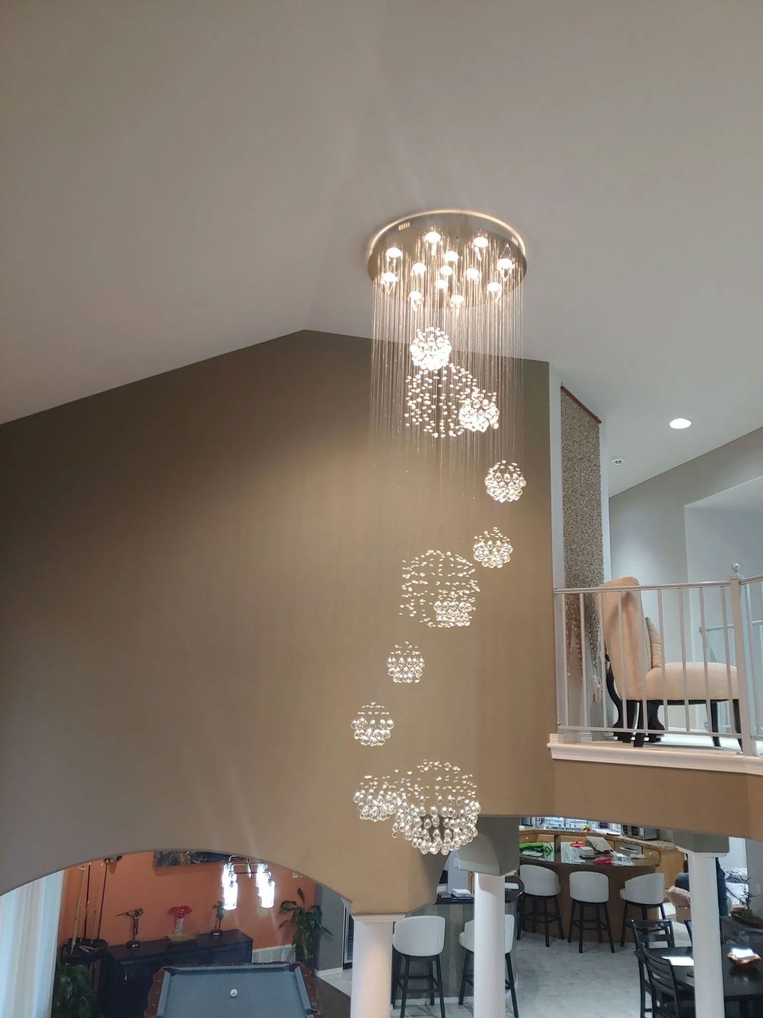 A modern chandelier hangs in a two-story foyer. The light fixture has many glowing spherical lights.